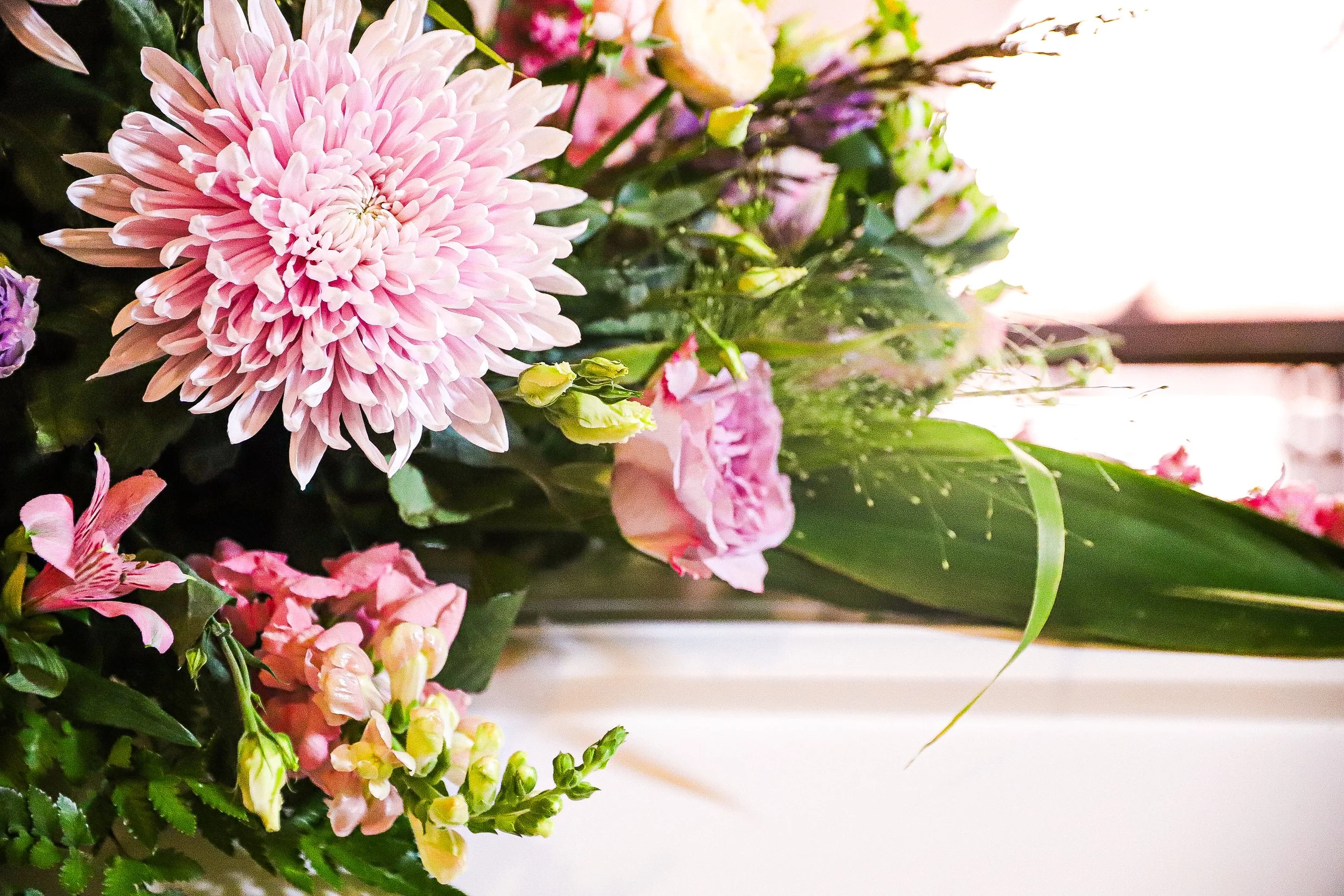 En bukett av blommor med stora rosa och vita blommor, inklusive en stor nätt rosa blomma i fokus, omgiven av mindre blommor och gröna blad.