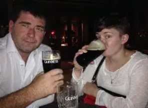 A man and woman sitting at a table in a pub, each holding a pint of Guinness beer.