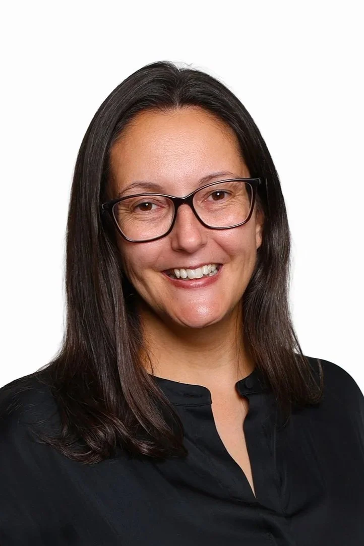 Headshot of Nicole Foster, a woman with dark brown hair, glasses, and a black top smiling against a white background.