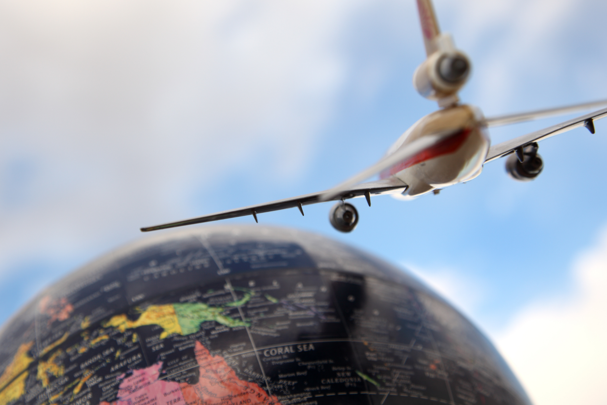 Close-up of a toy airplane flying above a globe map, with the sky in the background.