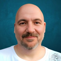 A picture of a middle aged man, bald head and beard, smiling at the camera