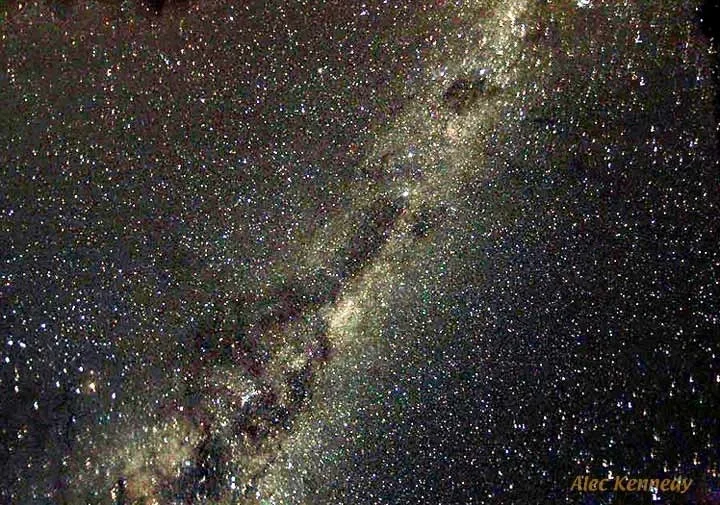 A night sky filled with stars and the Milky Way galaxy, with a dark landscape silhouette at the horizon.