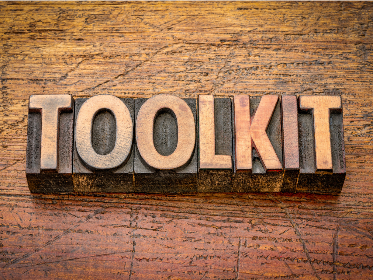 Letterpress blocks spelling 'TOOLKIT' on a wooden surface.