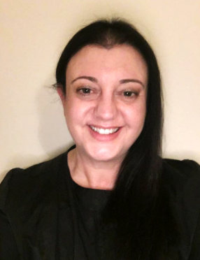 A woman with long dark hair smiling at the camera, wearing a black top, against a plain light background.