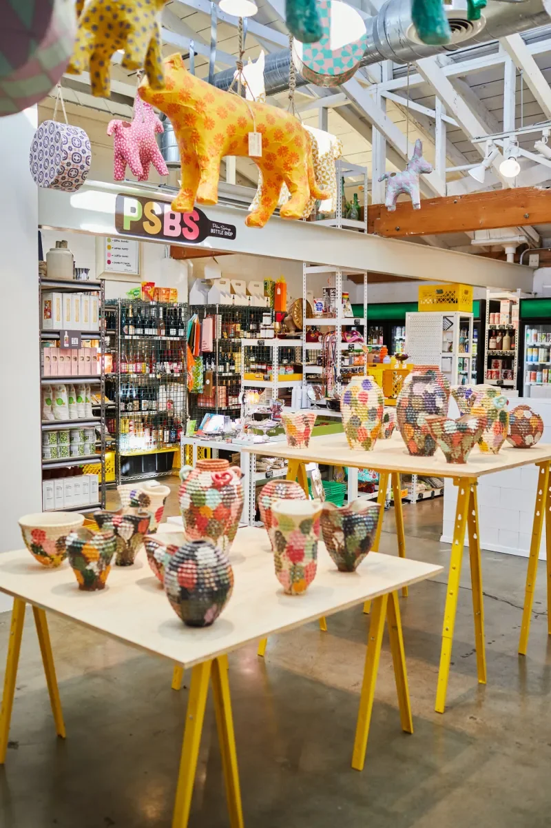 Colorful mosaic-patterned vases on display tables in a store with plush stuffed animals hanging above.