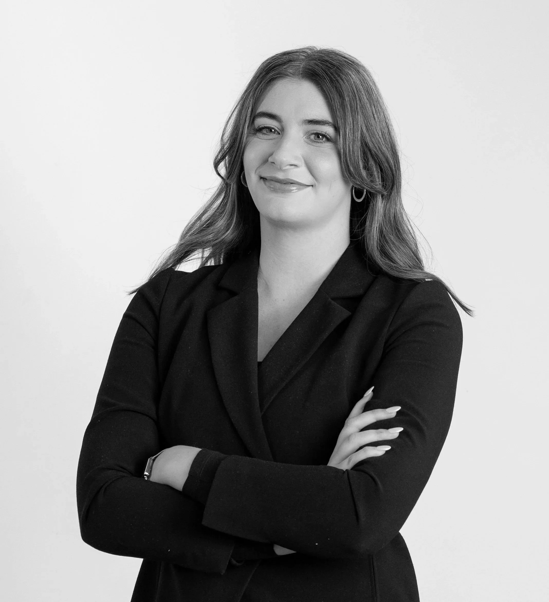 Black and white portrait of a woman with long hair, wearing a blazer, smiling with arms crossed, against a plain background.