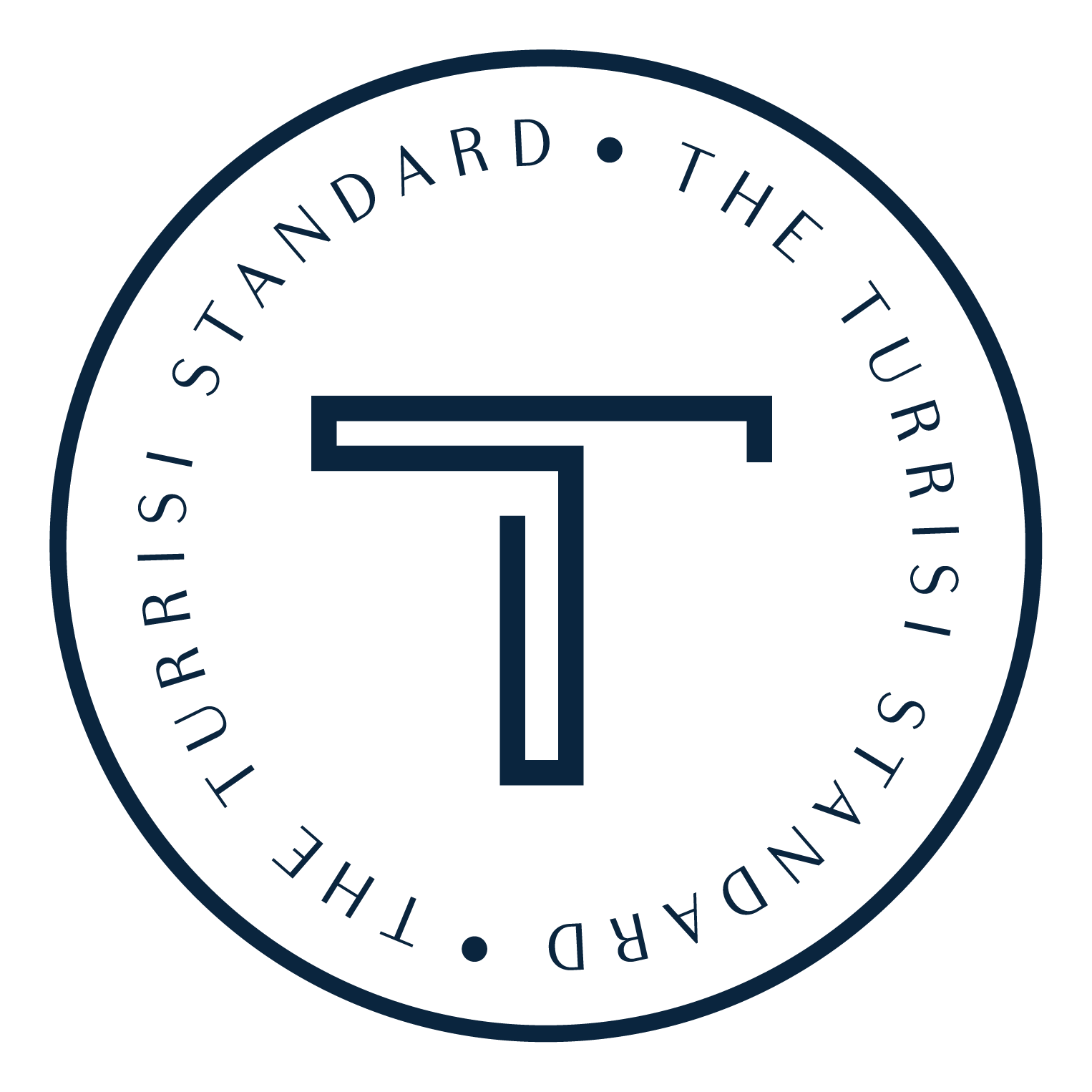 Circular logo with a large stylized letter 'T' in the center. Surrounding the letter is a ring of text that reads: 'THE STANDARD • THE TOUR RISING'.