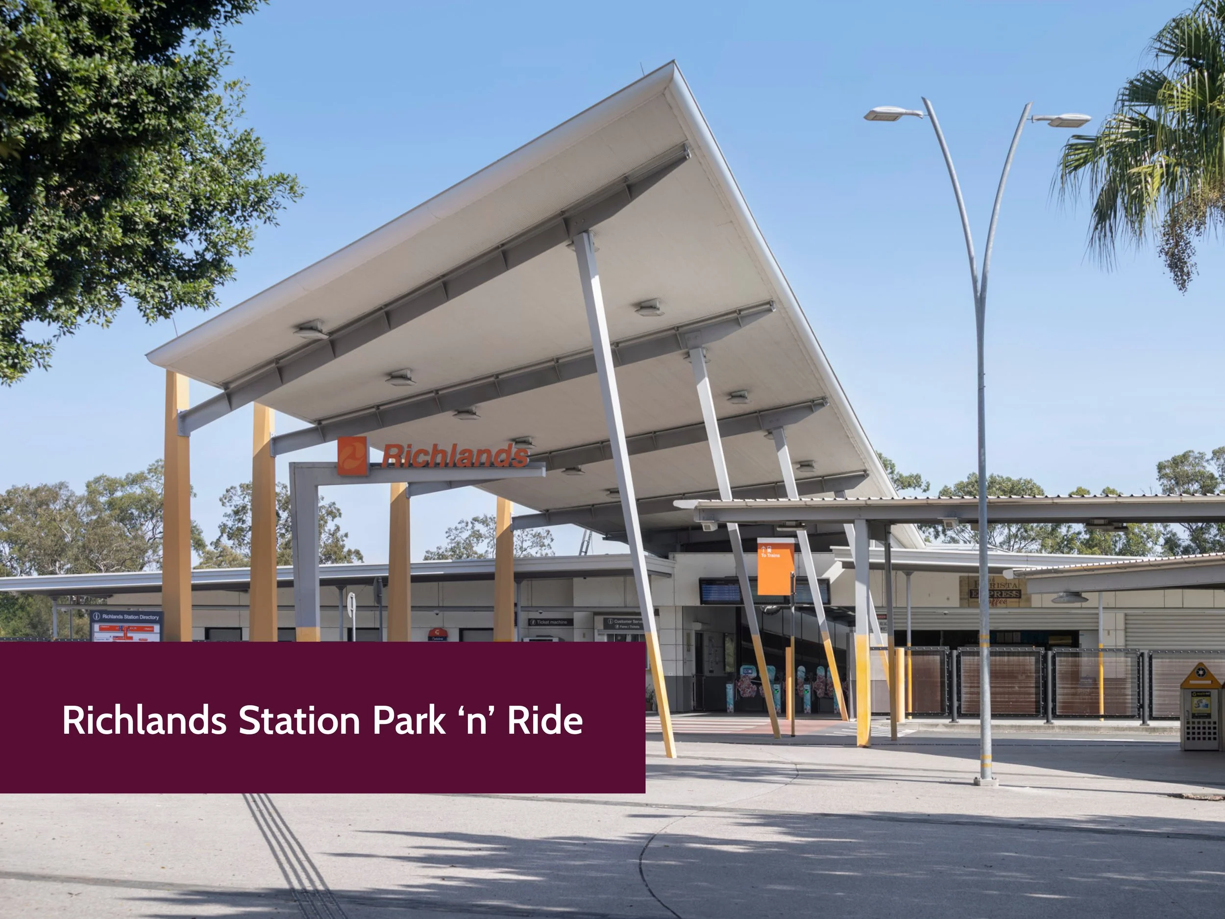 Exterior view of Richlands Station with a modern canopy structure, digital signs, and nearby trees, under a clear blue sky.