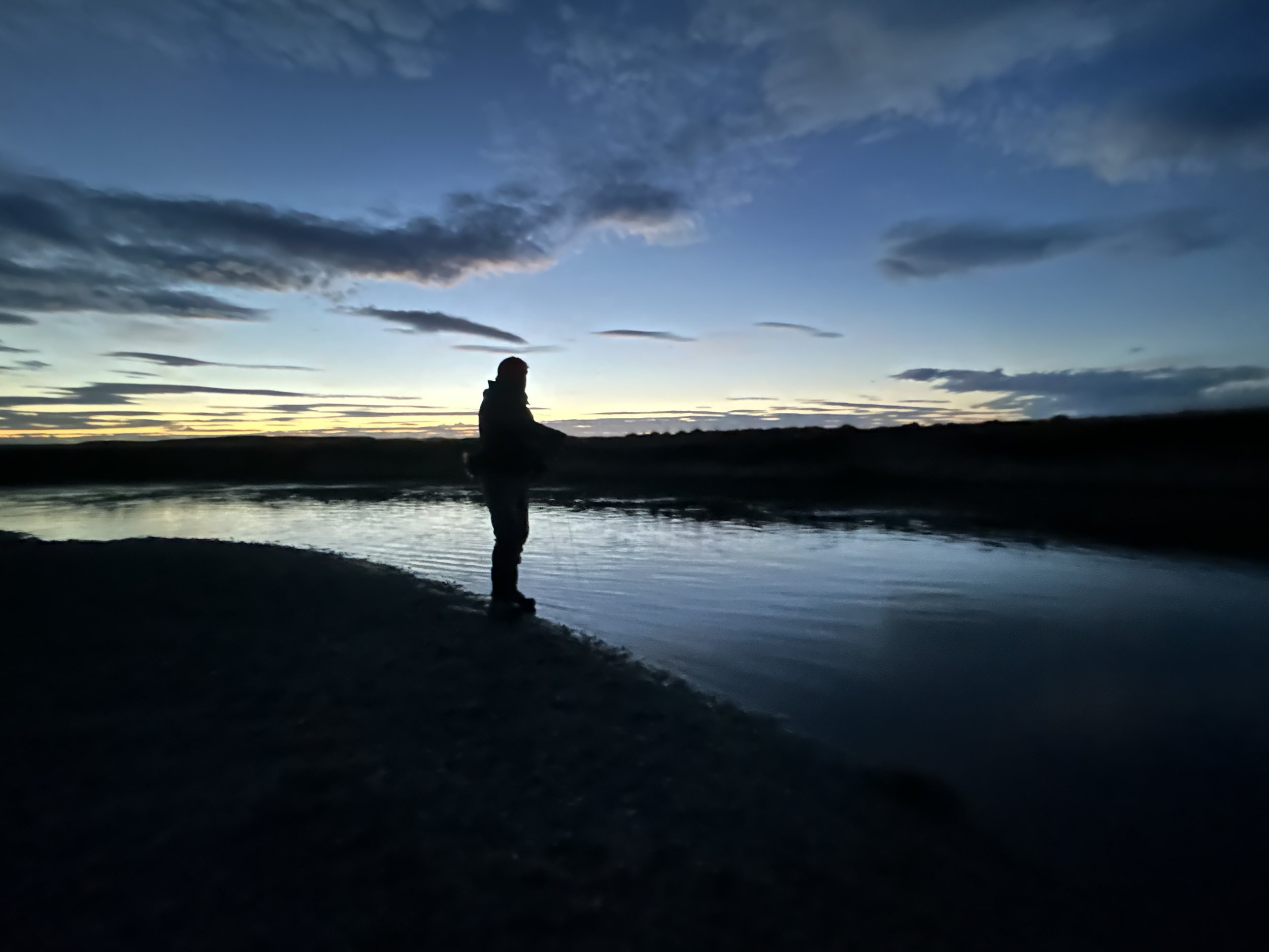 A fly angler beside a river at dusk