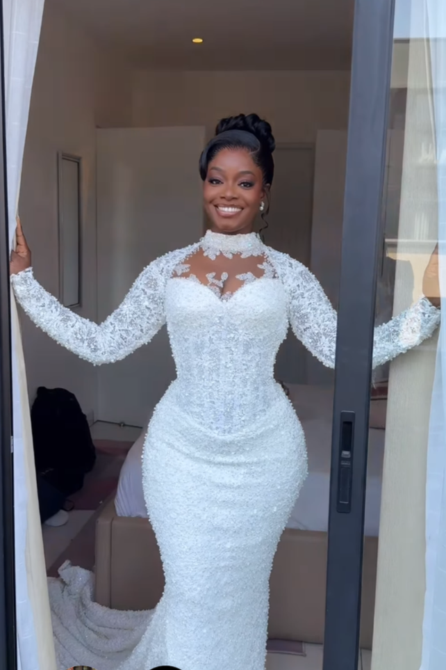 A woman in a white wedding dress standing in a doorway, smiling.