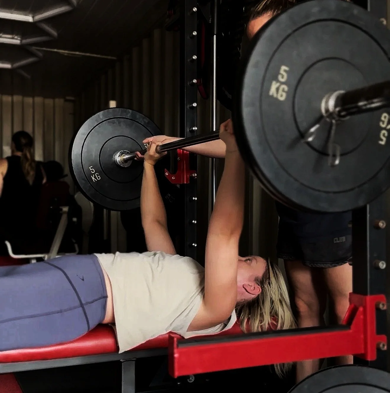 Womens Strength training class in Biggleswade and surrounding areas. A woman lying on a bench pressing a barbell with heavy weights at a gym.