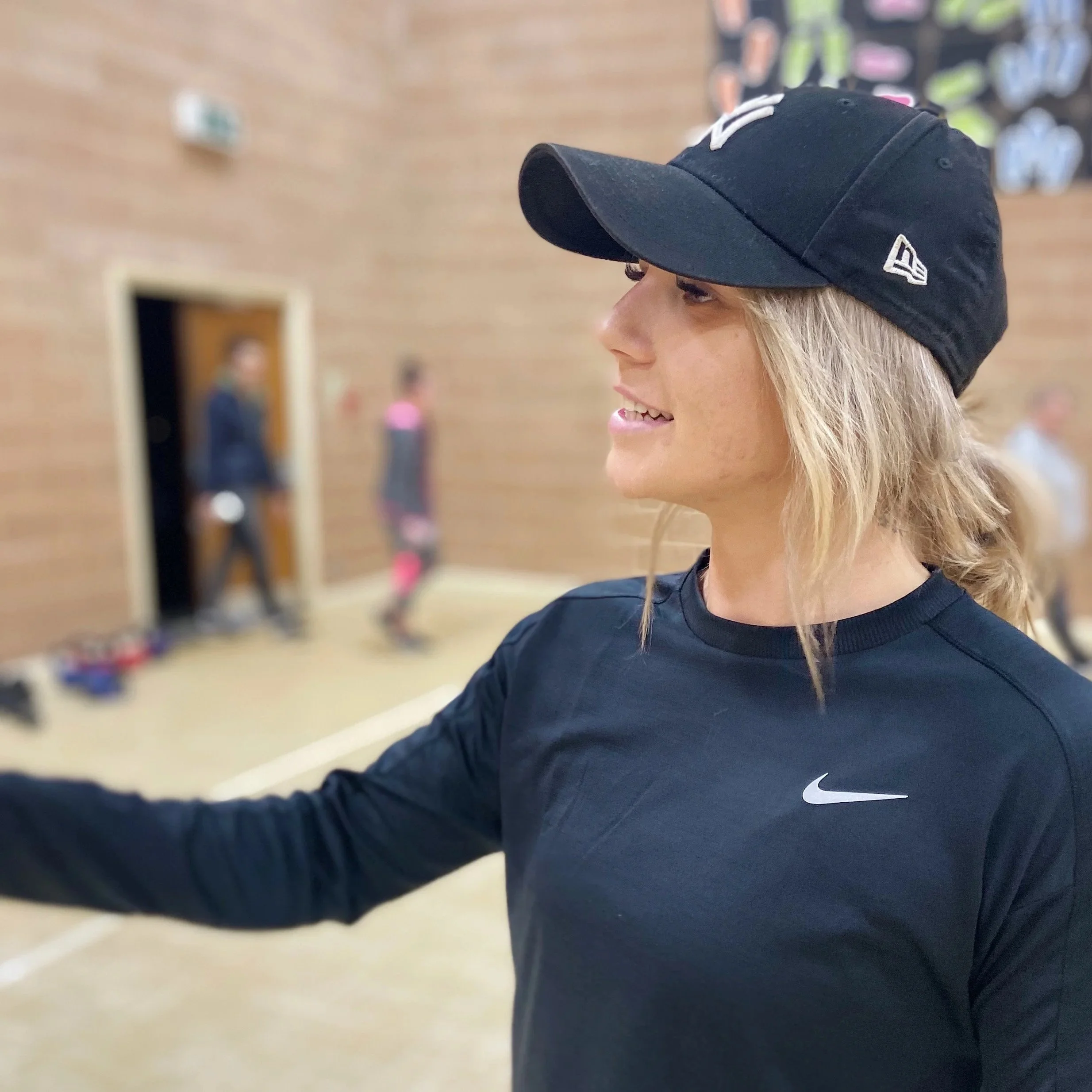 Close-up profile of a fitness coach instructing with a background of a gym or sports facility.