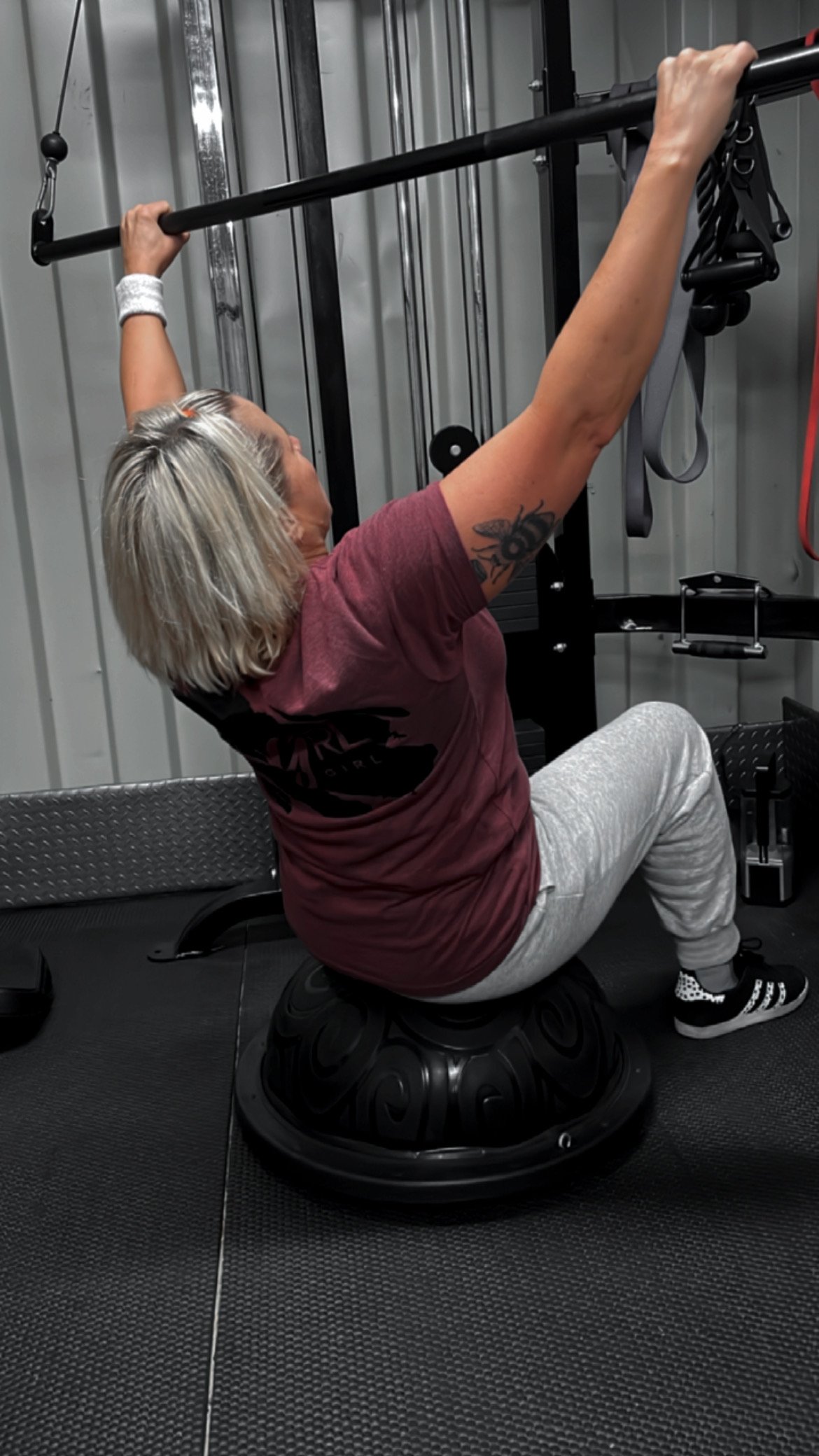 A woman with blonde hair wearing a strong girl t-shirt using gym equipment. 