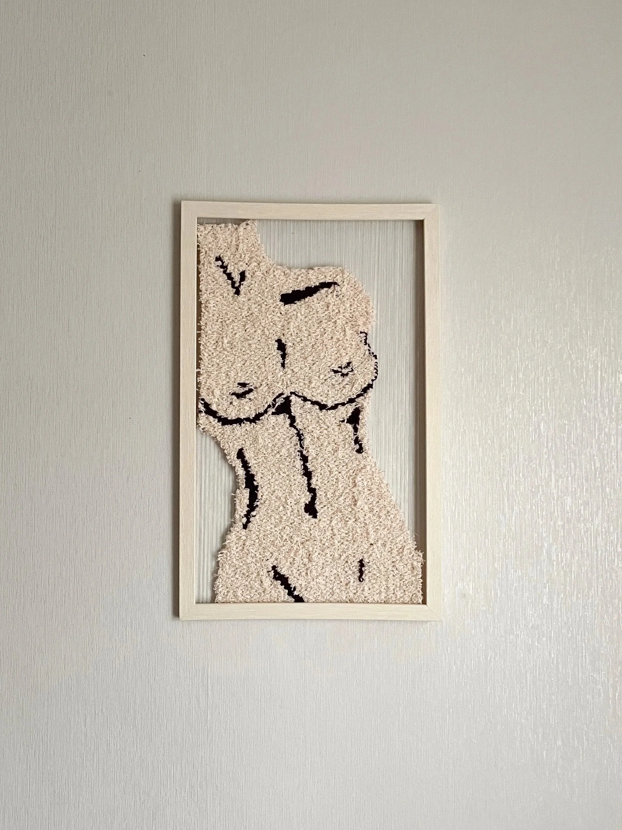 A framed textile art piece of a Shepherd Mix dog silhouette on a textured beige background, hanging on a plain light-colored wall.