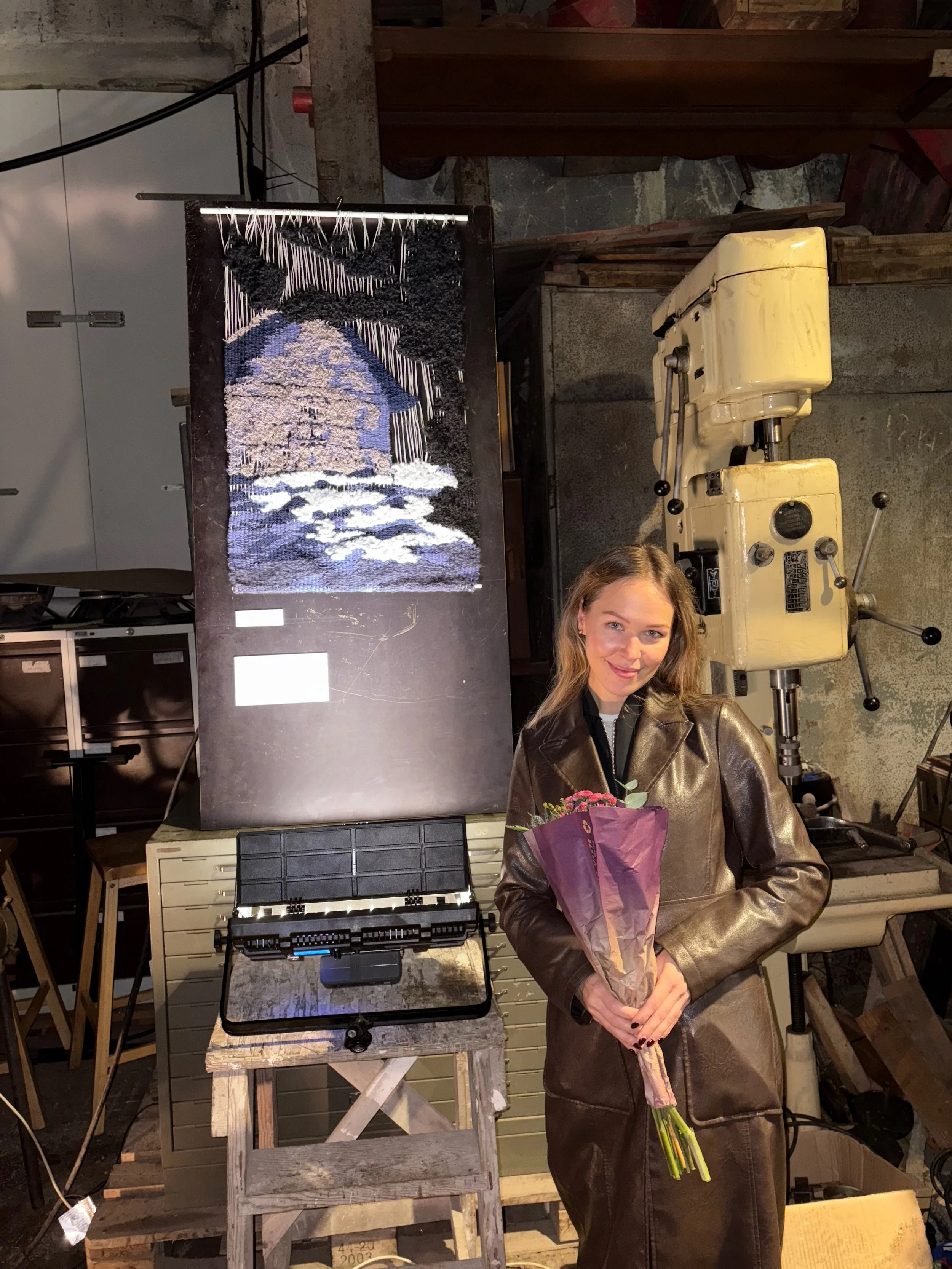 Woman holding a bouquet of flowers standing with a textured artwork on display on the wall.