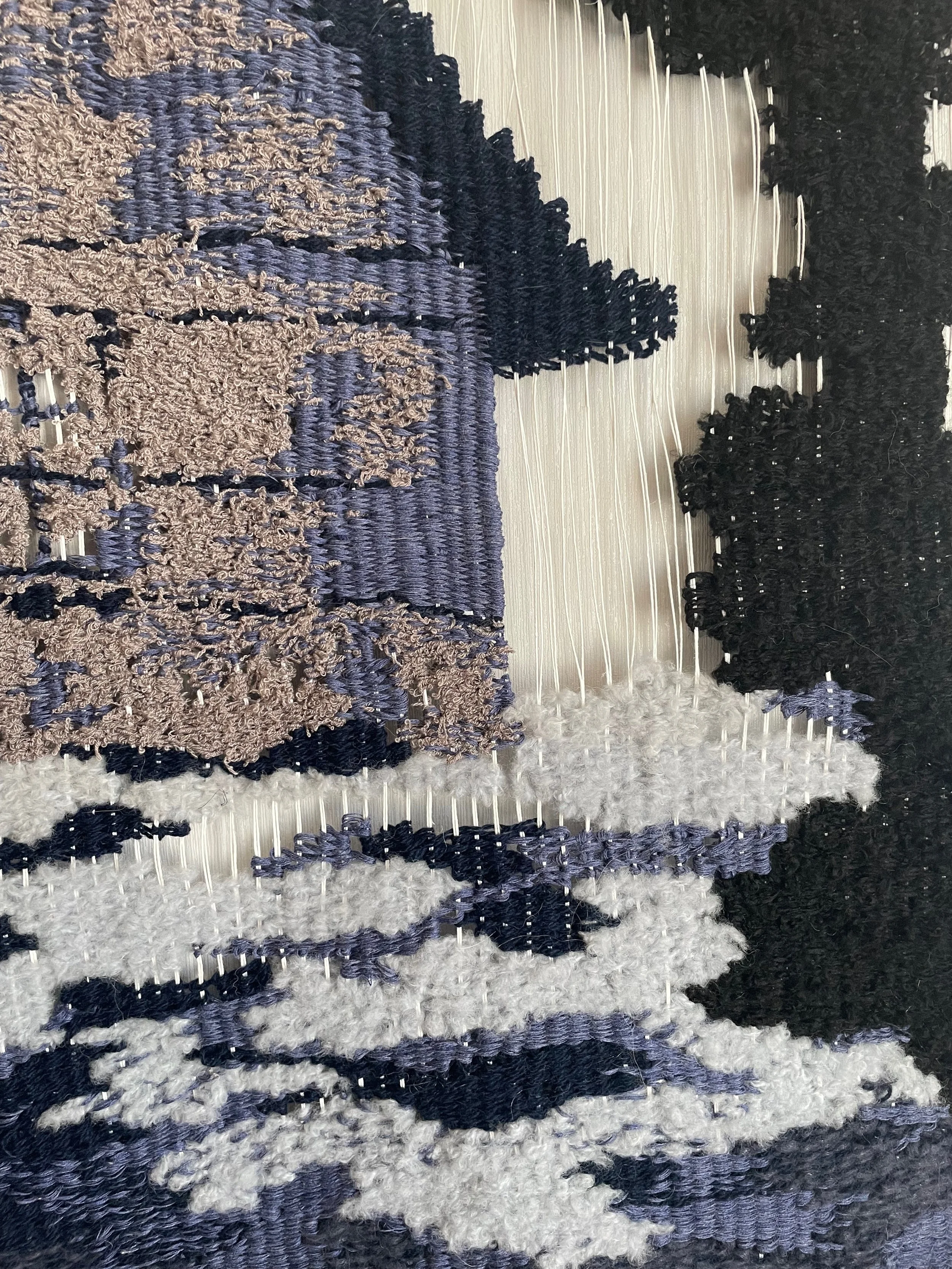 Close-up view of woven fabric with shapes made from beige, gray, black, and white yarns.