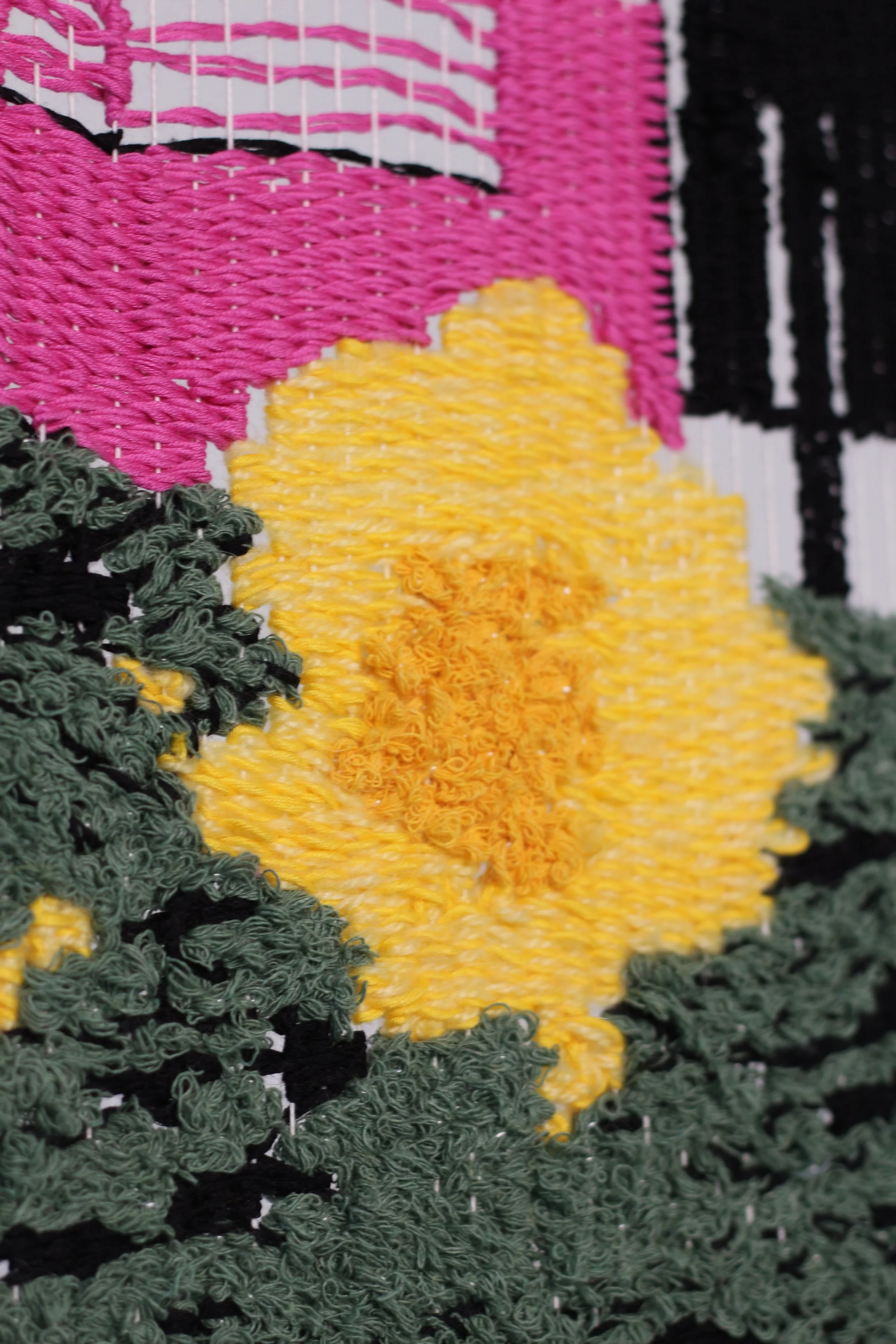 A close-up of a textured woven textile artwork featuring yellow, pink, black, and green thread forming a colorful image.