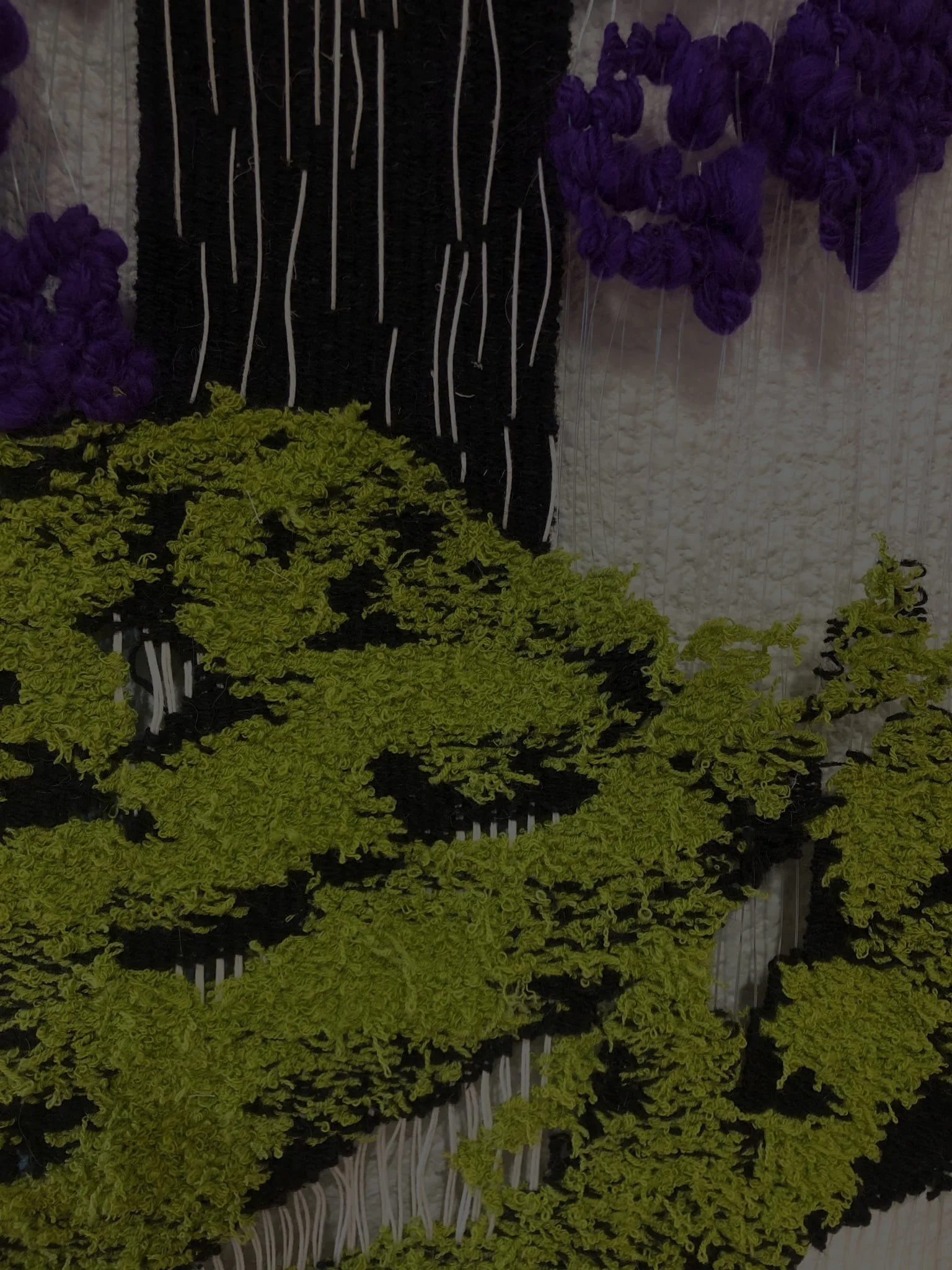 Close up of a woven tapestry with purple, black and green fragments and yarns.