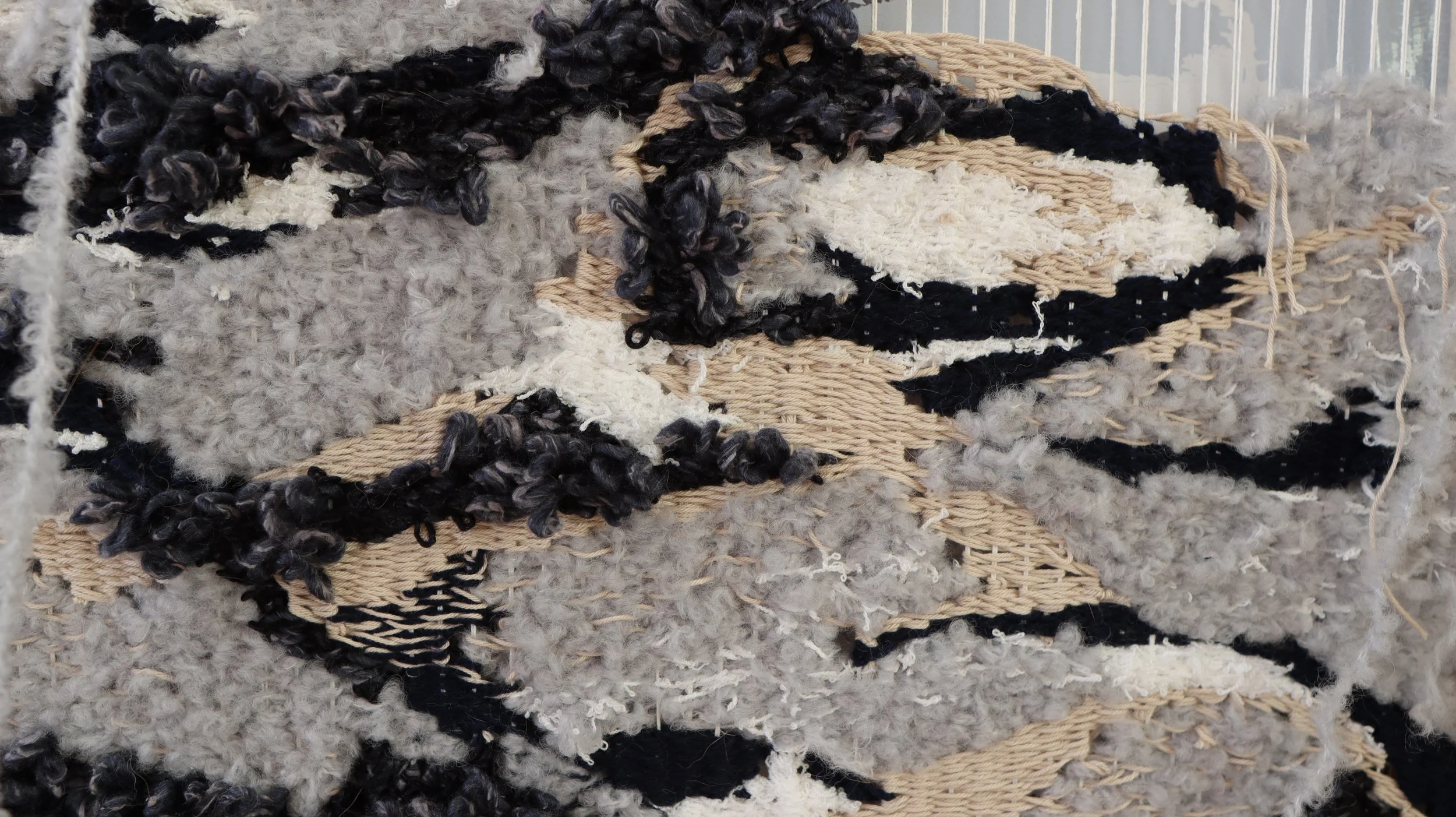 Close-up of a textured woven wall rug with black, white, beige, and gray fibers.