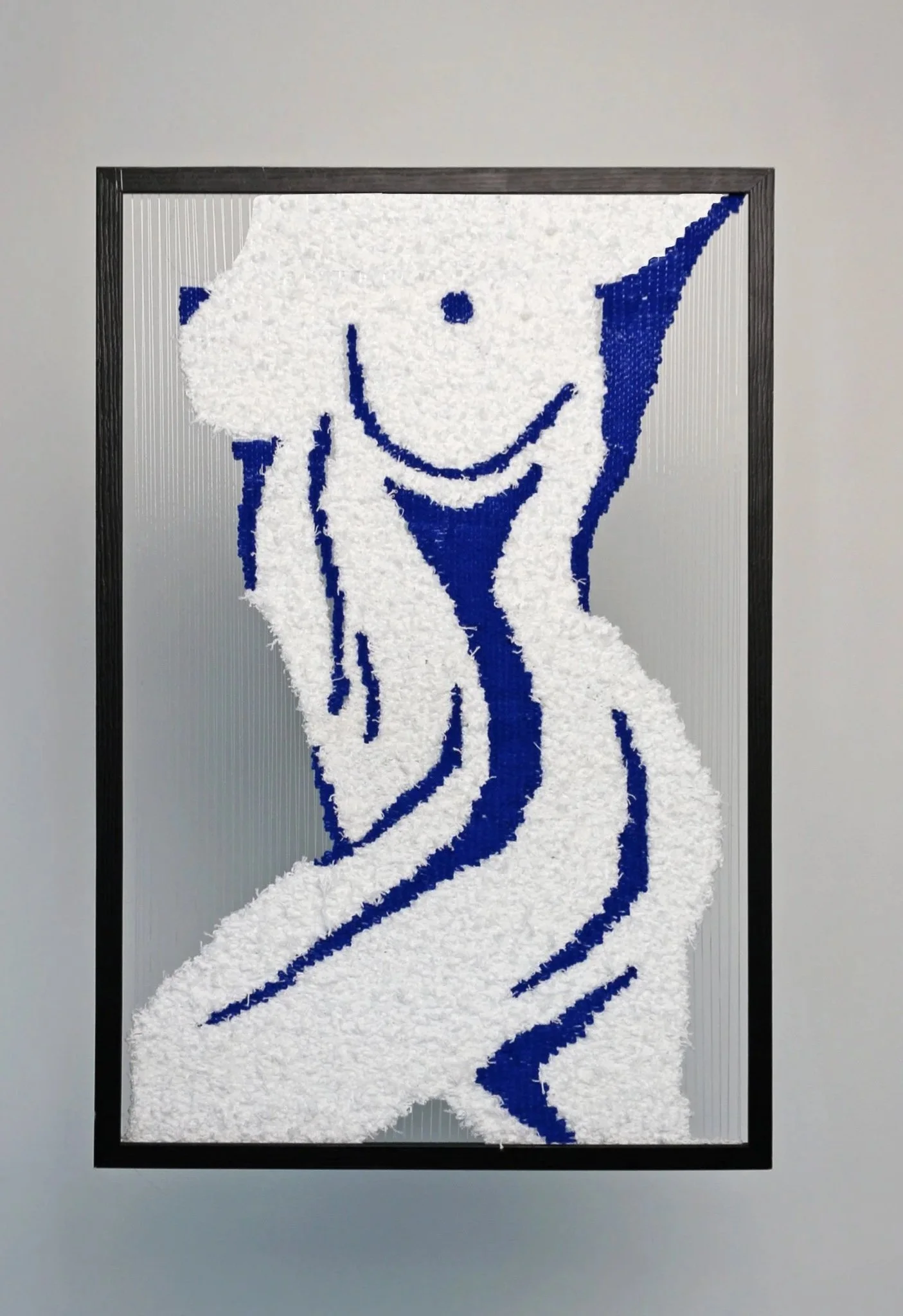 A framed artwork of a female figure with breasts made from white and blue textile materials.