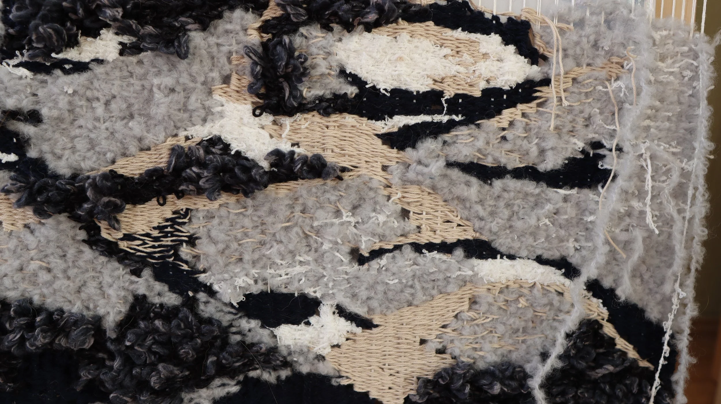 Close-up of a textured woven rug with a mix of beige, black, white, and gray fibers, featuring various knots and patterns.