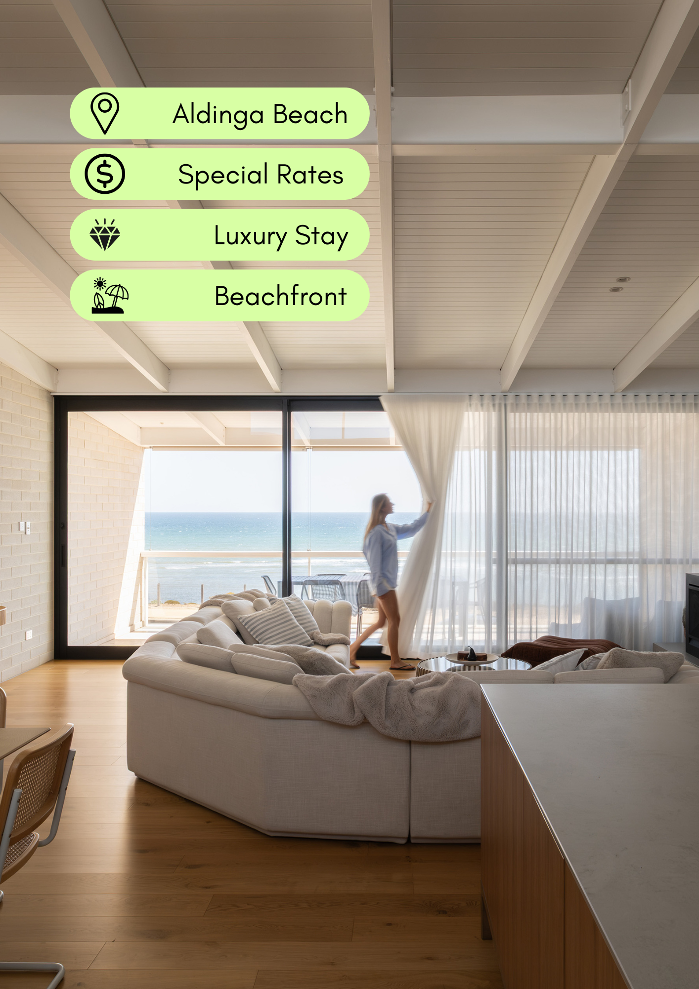Living room with a large cream sectional sofa, a woman opening a sheer curtain, ocean view outside, wooden floor, beige brick wall, and modern decor.