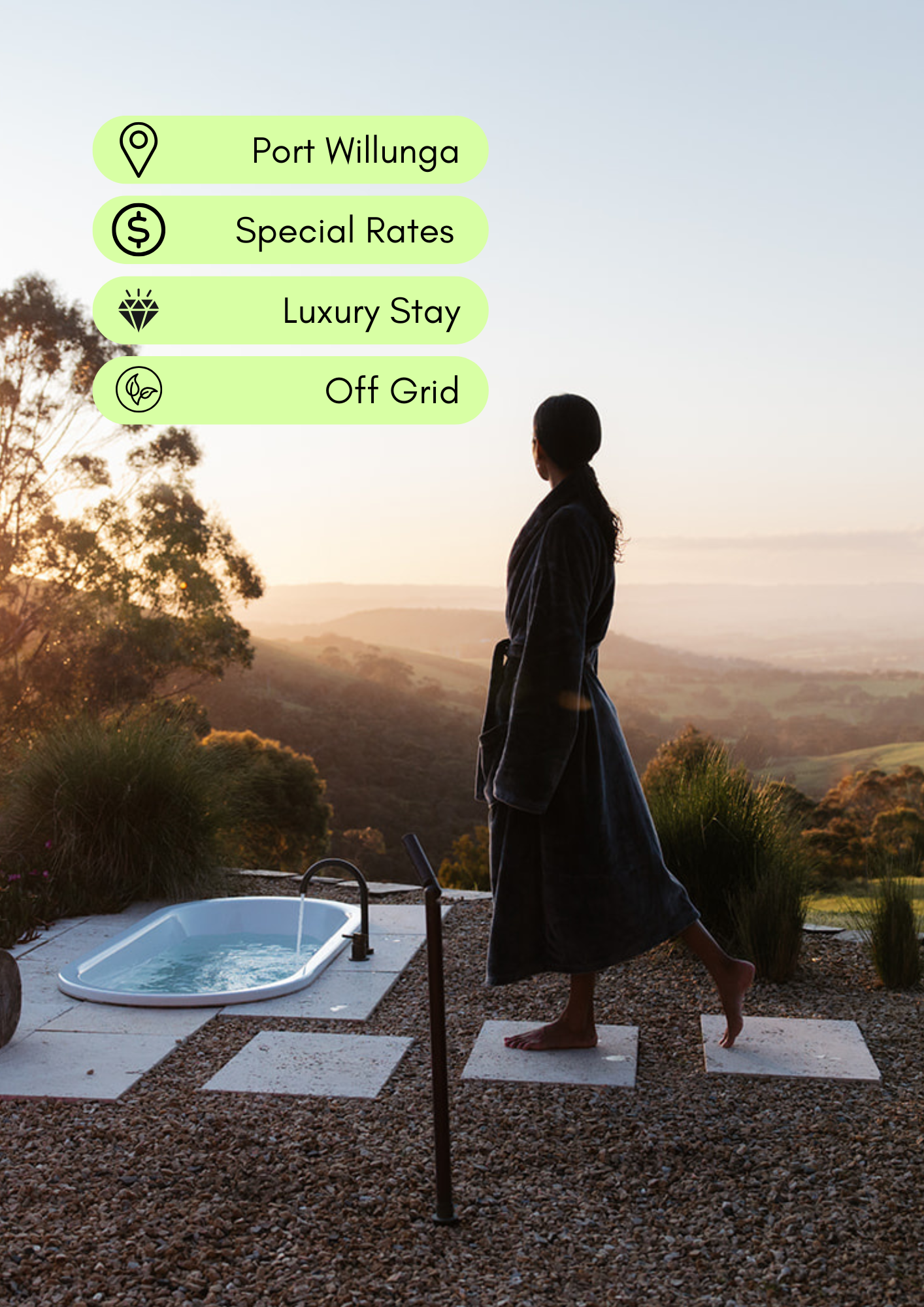 A woman stands on stepping stones outside by a hot tub at sunset, overlooking a scenic landscape with hills and trees.