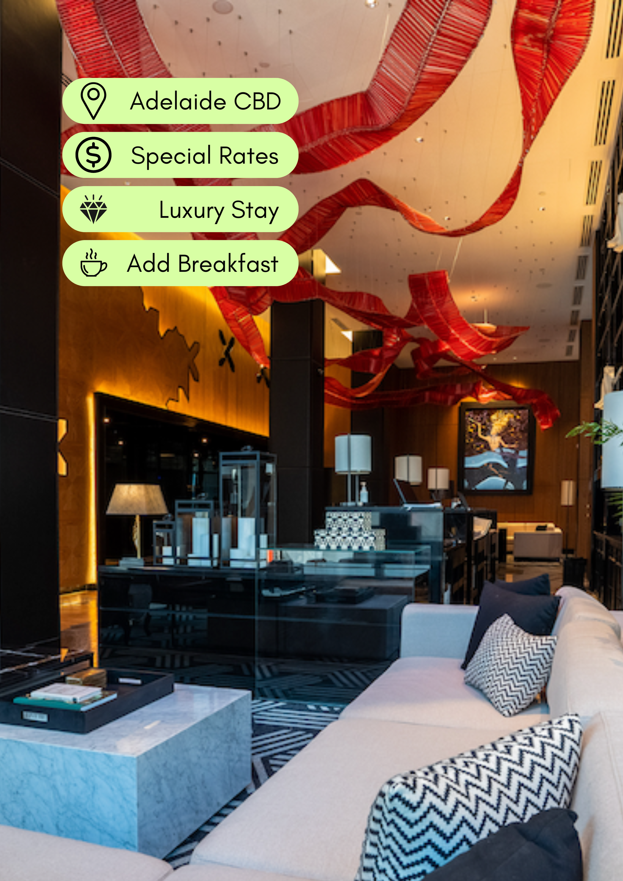 Modern hotel lobby with abstract red ribbon sculpture on ceiling, wooden walls, contemporary furniture including a beige sofa with black and white patterned pillows, a marble coffee table with books and a tray, and ambient lighting.