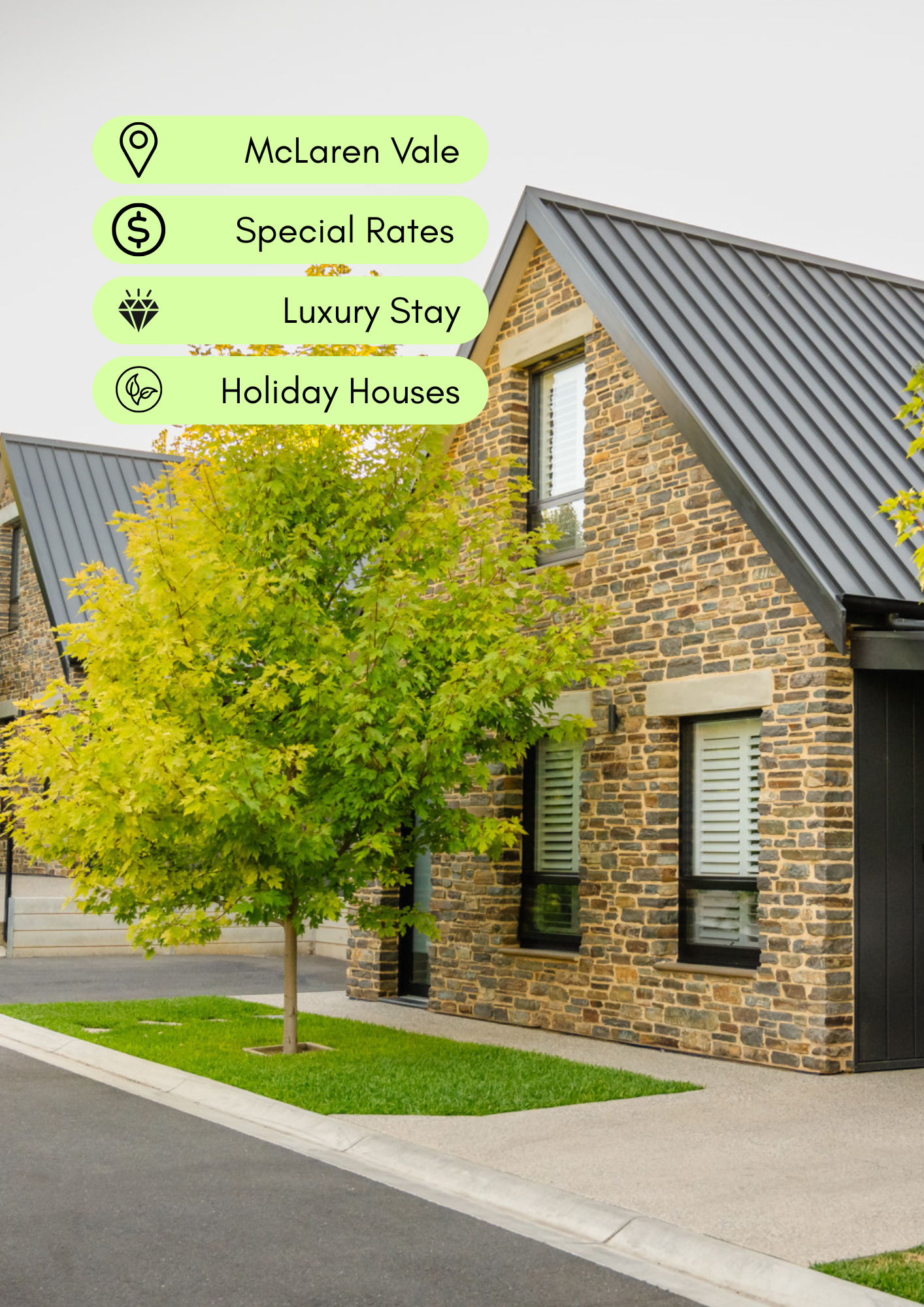 Street view of a modern brick house with black roof, green lawn, tree, and sidewalk.