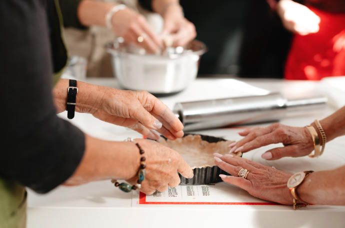 People making dough in a kitchen, using a rolling pin and a tart pan.