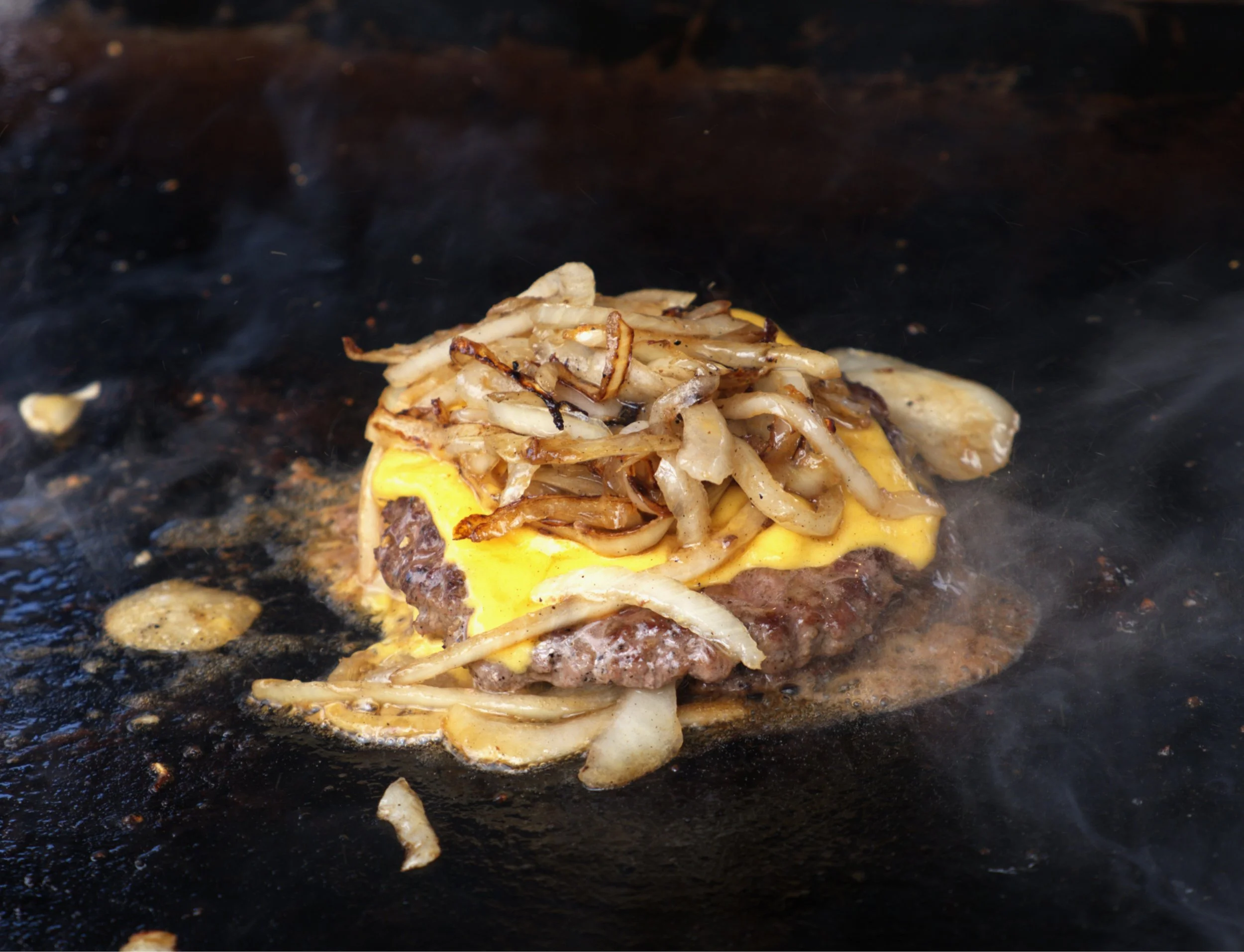 Cooking cheeseburger with sautéed onions on a griddle.