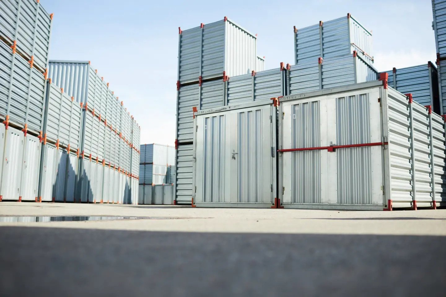 A storage yard filled with stacked metal shipping containers with closed doors, under a clear sky.