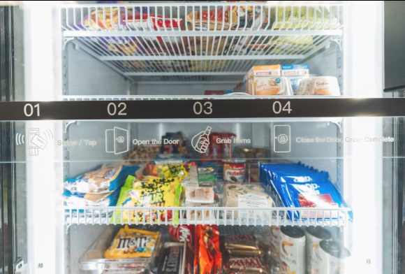 Inside a vending machine stocked with various snack items including chips, candy bars, and bottled drinks, with instructions to swipe, open door, grab items, and close door.