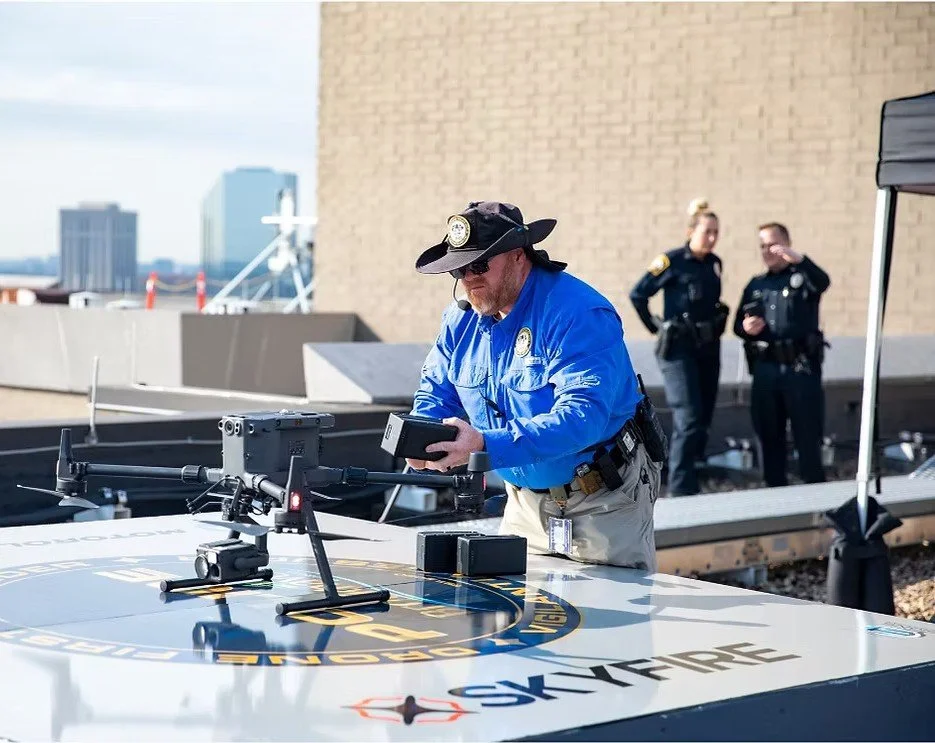 Police officers operating a drone on a rooftop with a cityscape in the background.