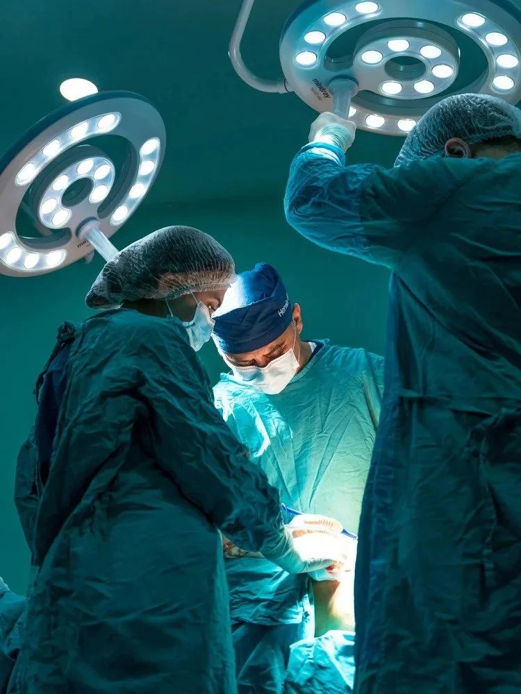 Surgeons in protective gear performing an operation under bright surgical lights in an operating room.