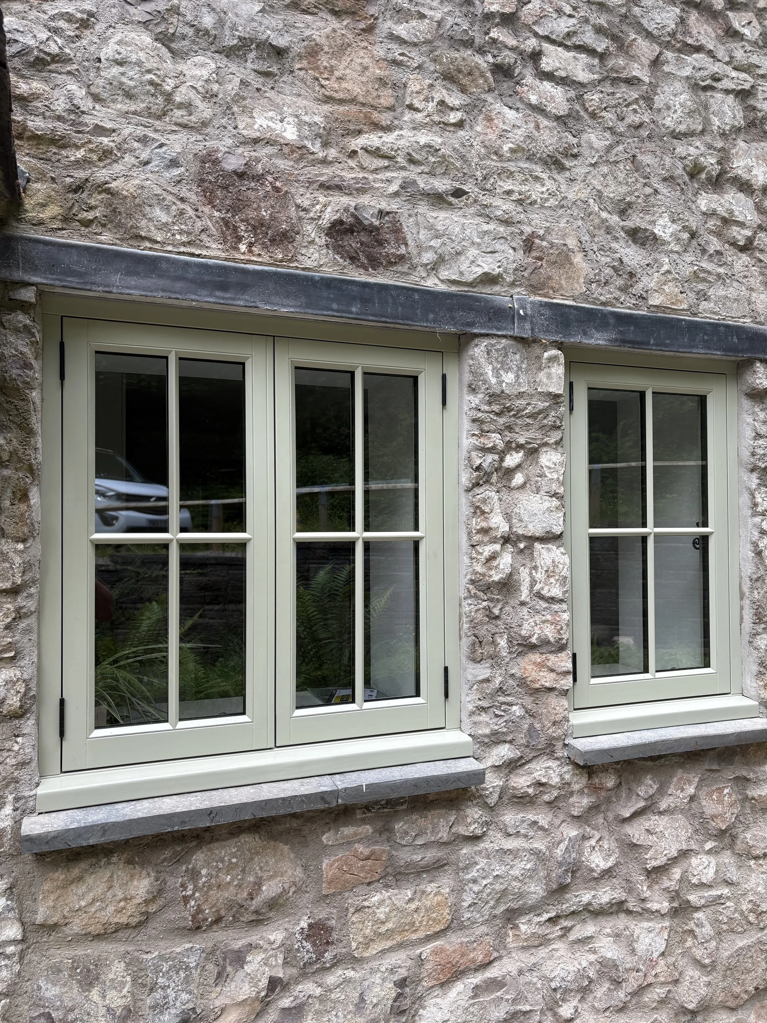 A stone exterior wall with two cream-colored framed windows, each with multiple panes, and gray stone window sills. in Flintshire