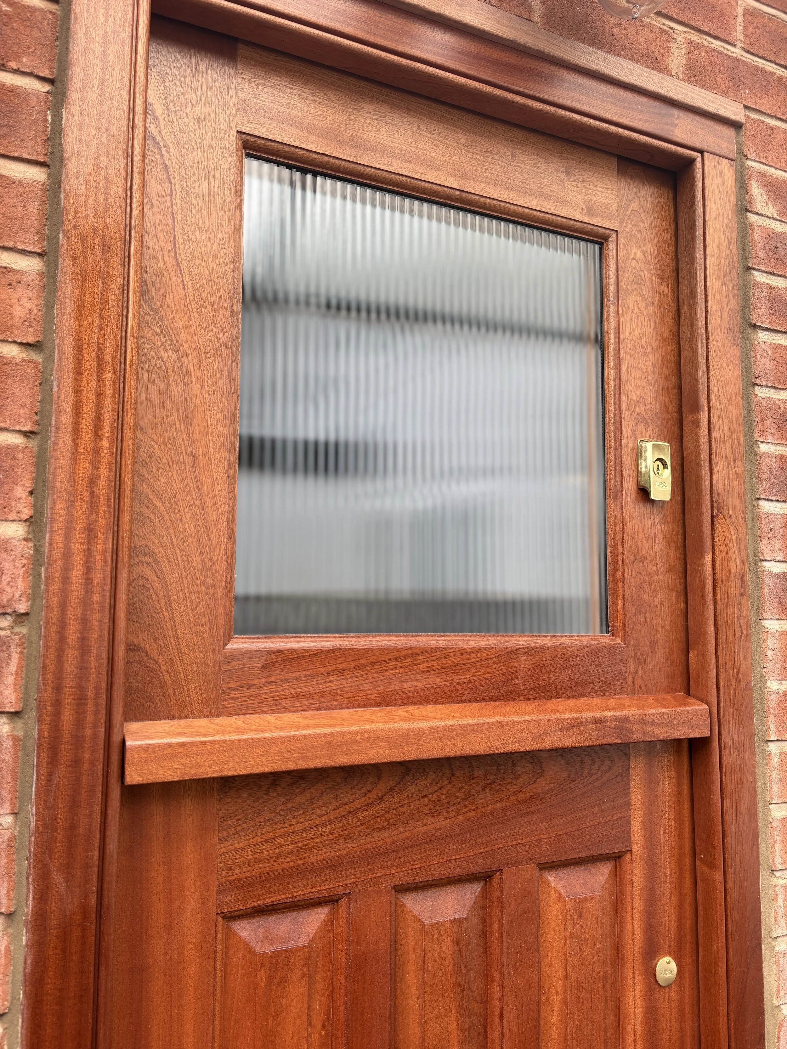 A wooden door with a glass window, a brass lock, and brick wall surrounding it. in Cheshire 
