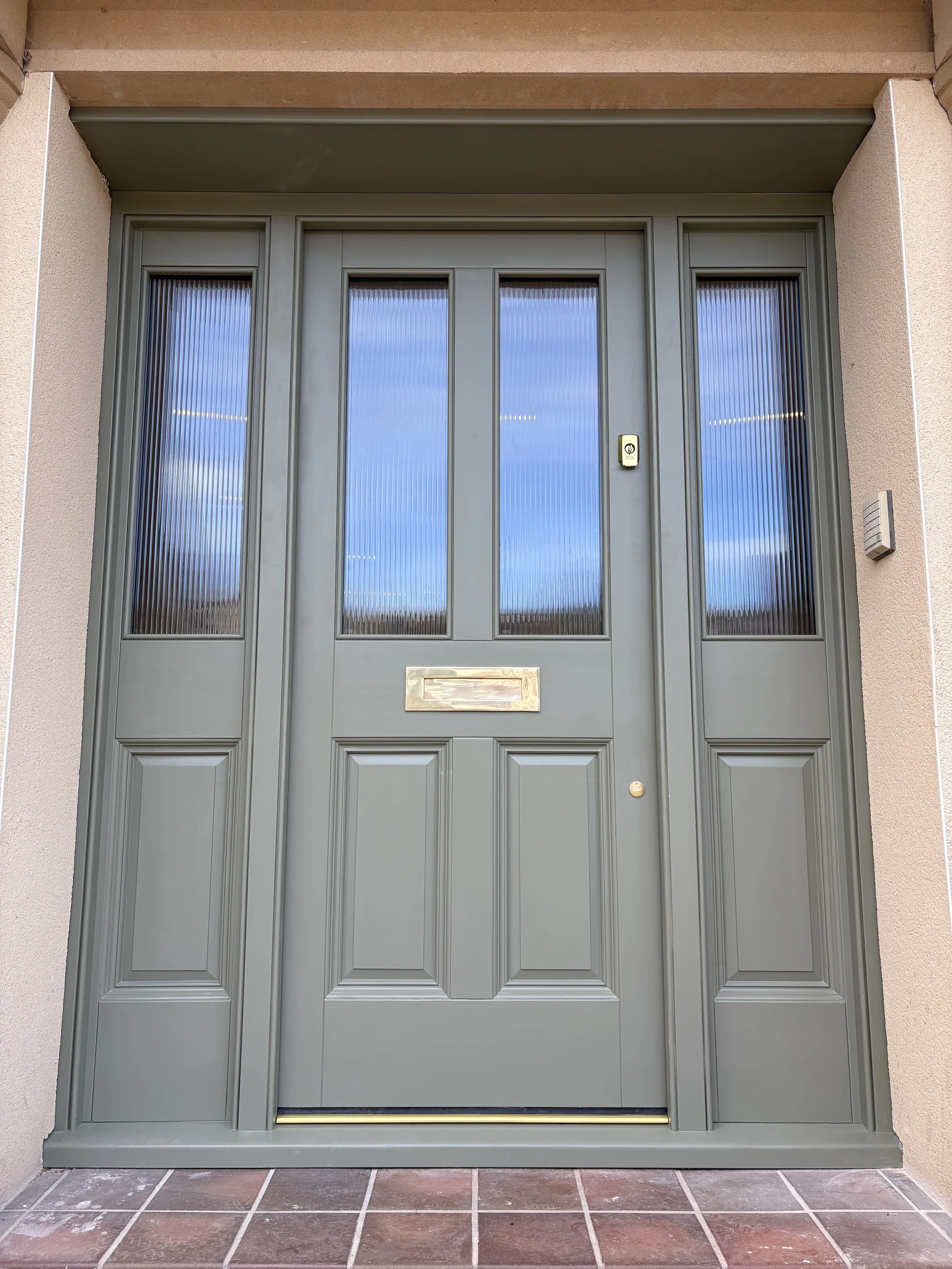 Green front door with glass panels and a mail slot, flanked by beige walls and tile flooring. in Chester