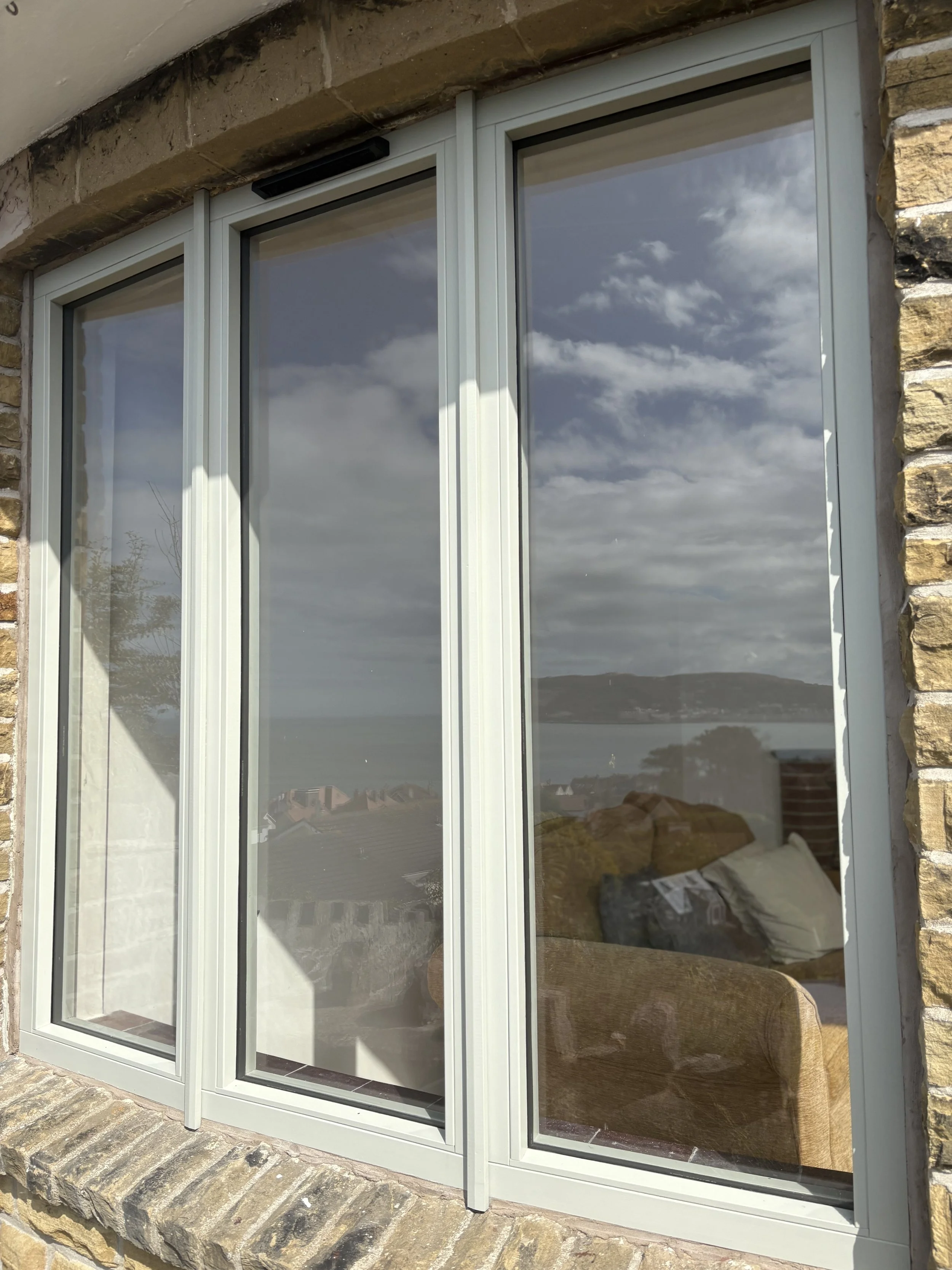 A large window with a white frame set in a stone wall, reflecting cloudy sky and distant landscape. in Handbridge