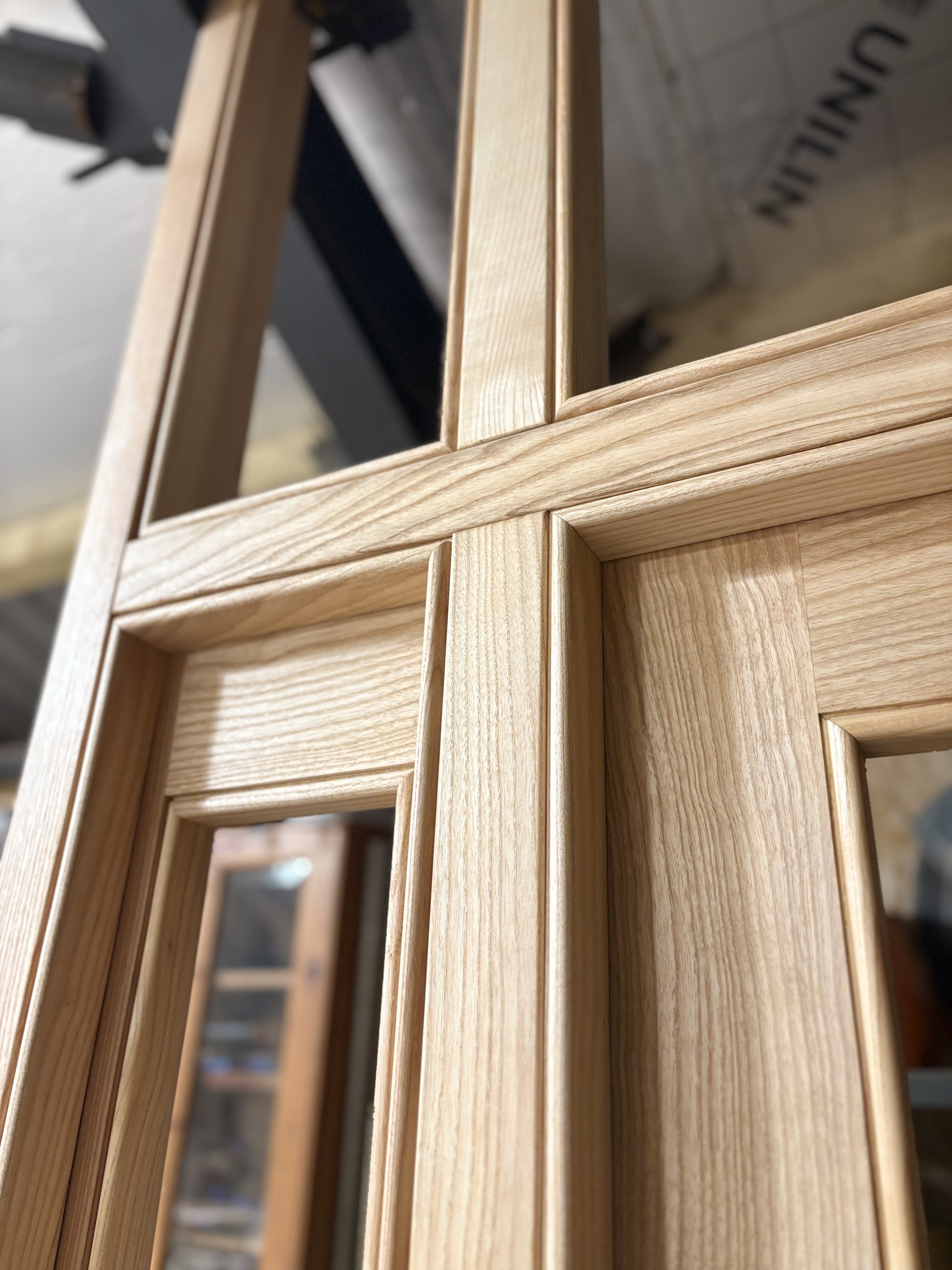 Close-up of unfinished wooden window frame with multiple panes, showing detailed wood grain and craftsmanship.