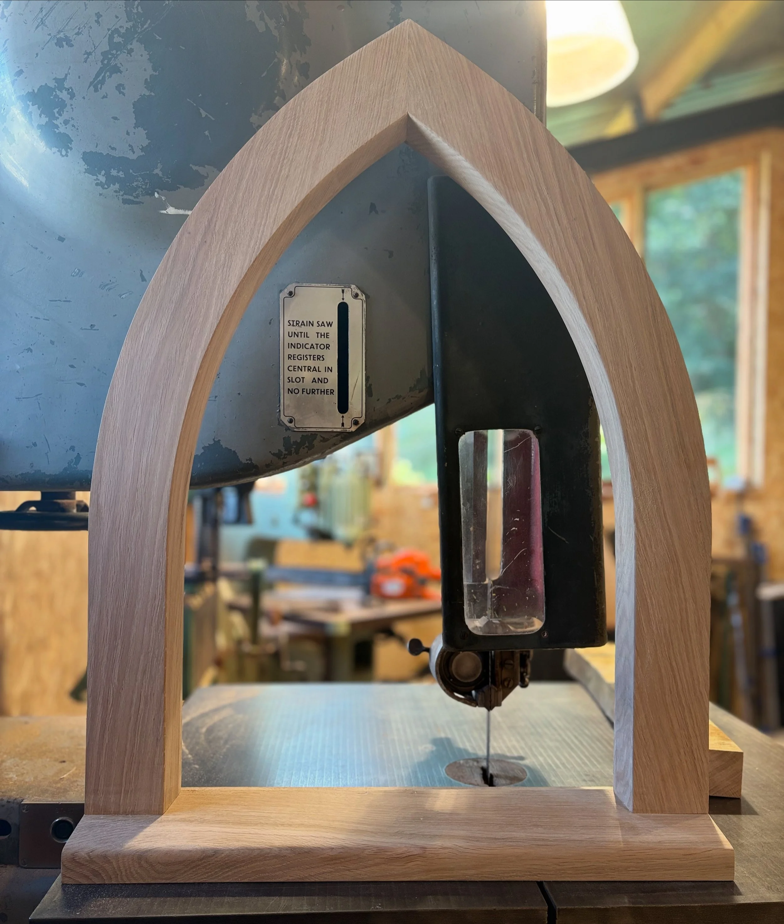 A wooden arch structure with a metal mechanical component inside, mounted on a wooden stand, in a workshop setting with tools and wood in the background. made for a job in blacon