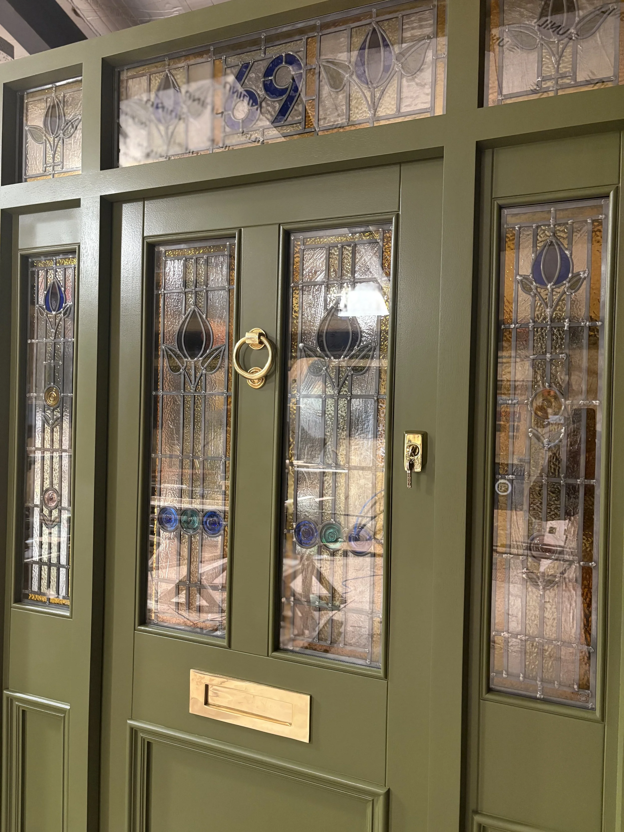 A green front door with decorative stained glass windows and a brass handle, a mail slot, and a lock. in Conwy