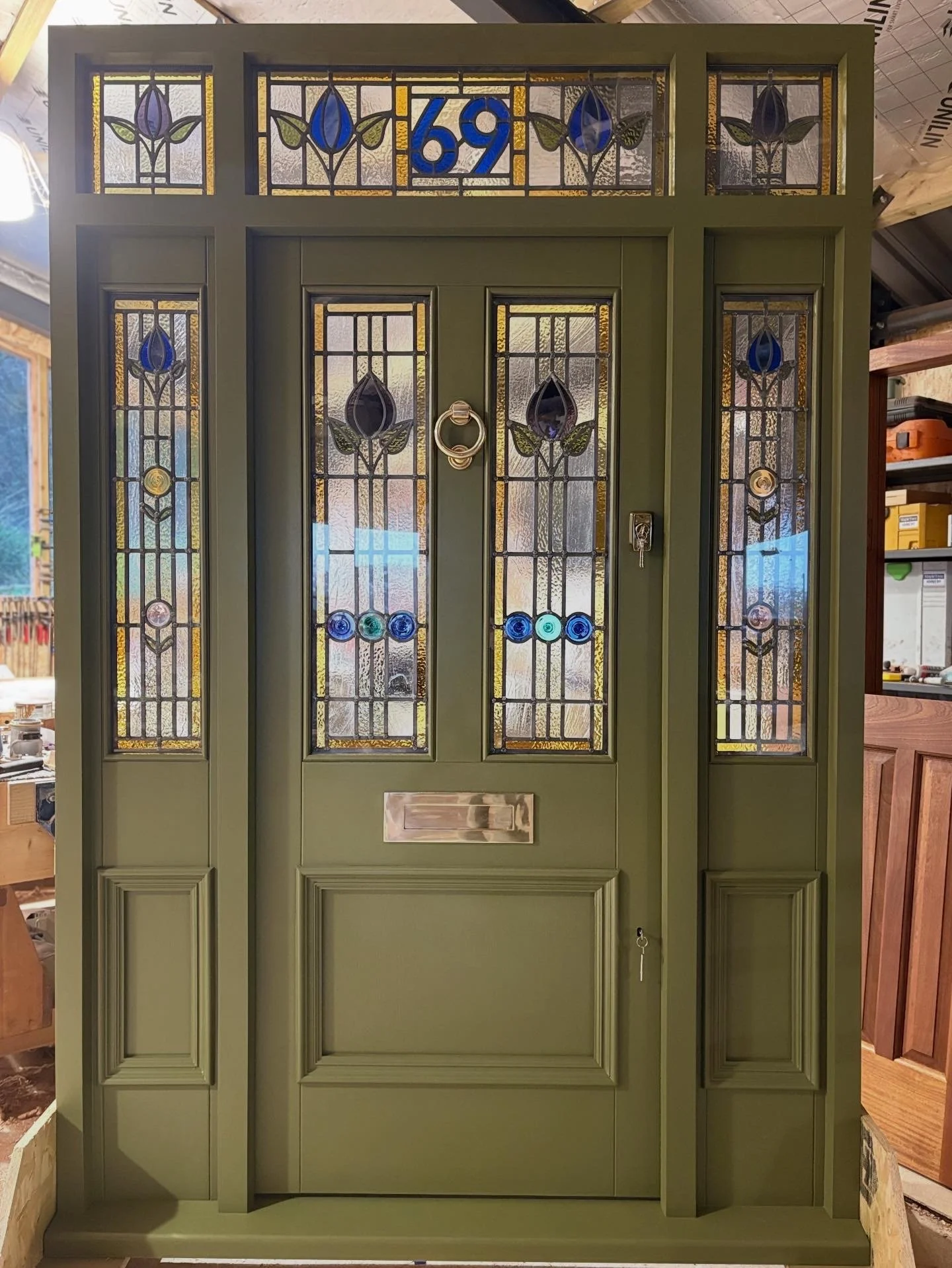 A green front door with stained glass windows featuring blue and purple flower designs, house number 169 above the door, a door knocker, and a mailbox slot.