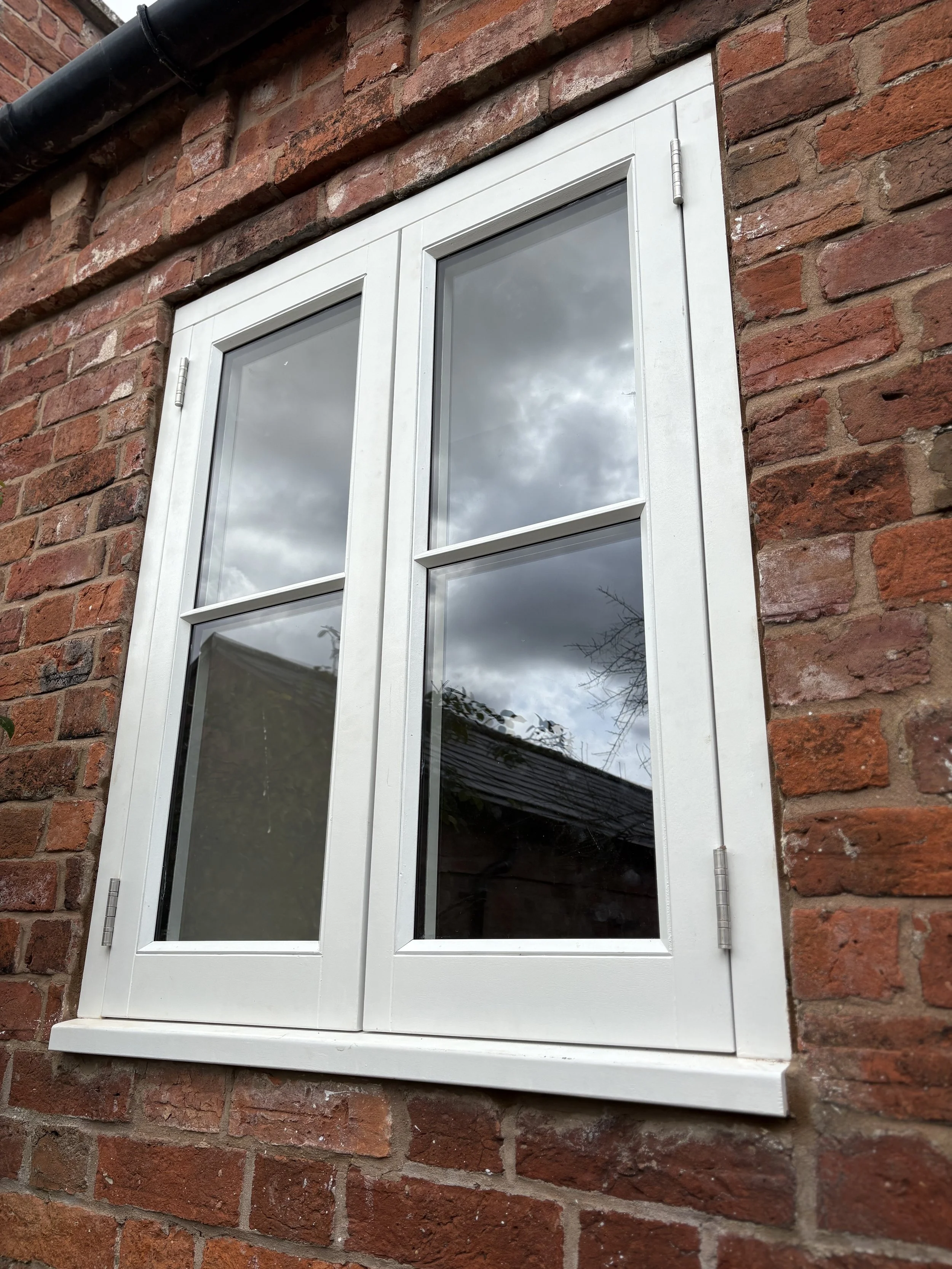 A white-framed window on a red brick wall, reflecting cloudy sky and trees.