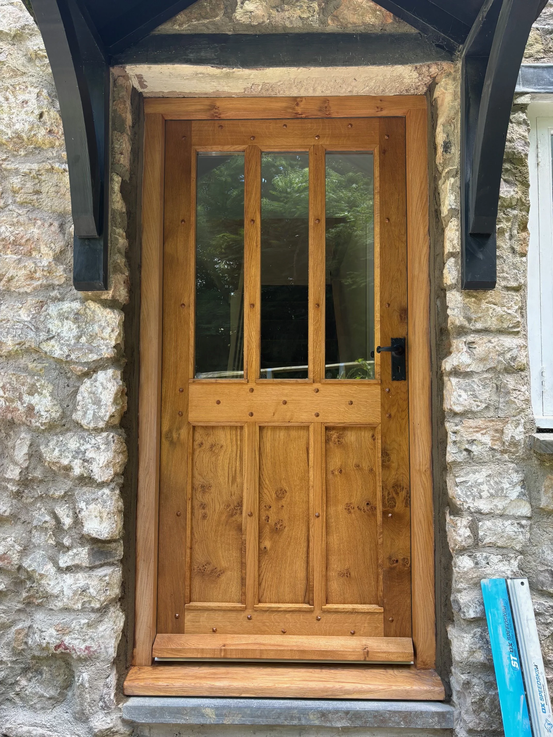 Wooden door with glass panels in a stone wall, black handle and latch, small blue box on ground to the right.
