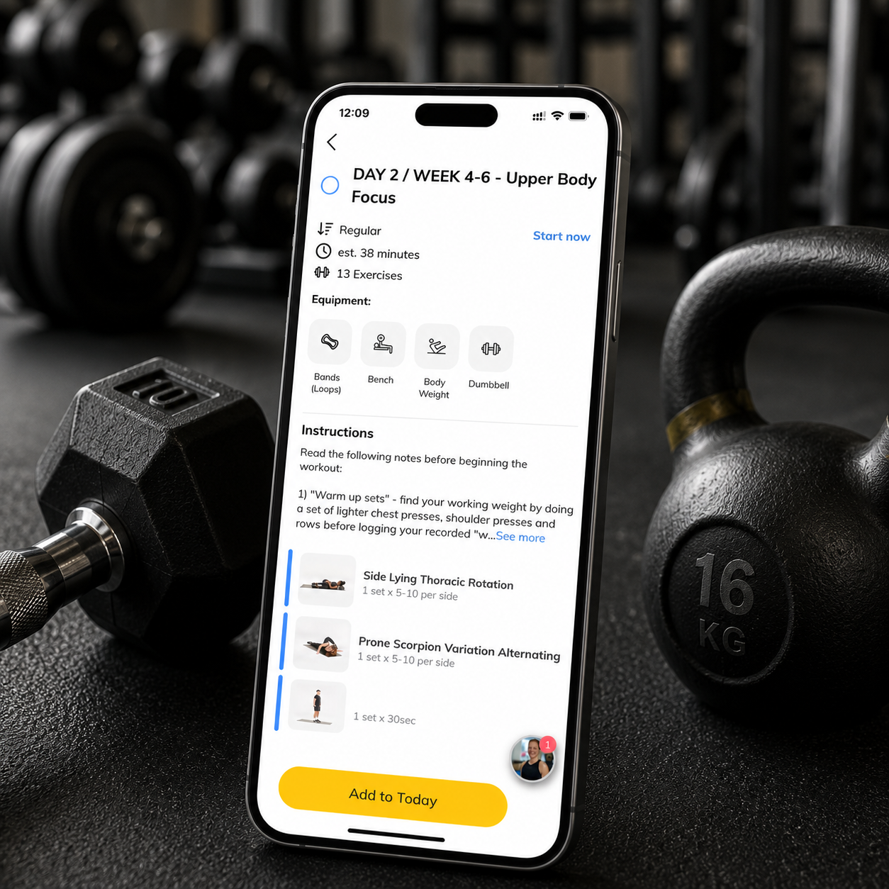 A smartphone displaying a workout app screen titled 'DAY 2 / WEEK 4-6 - Upper Body Focus' on a gym bench with a dumbbell and a kettlebell nearby.