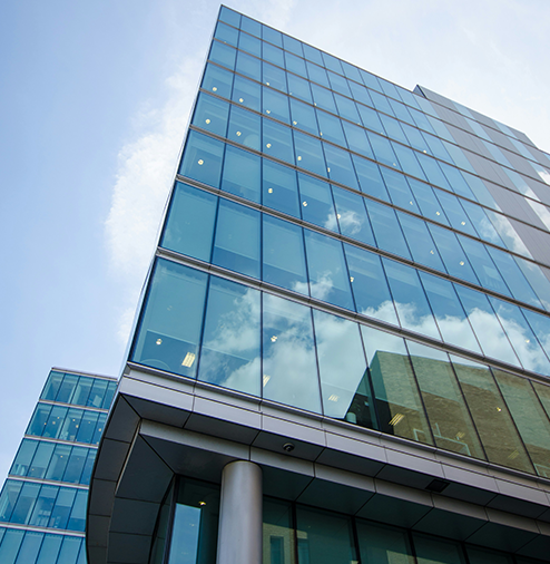 A modern glass office building reflecting the sky and clouds.