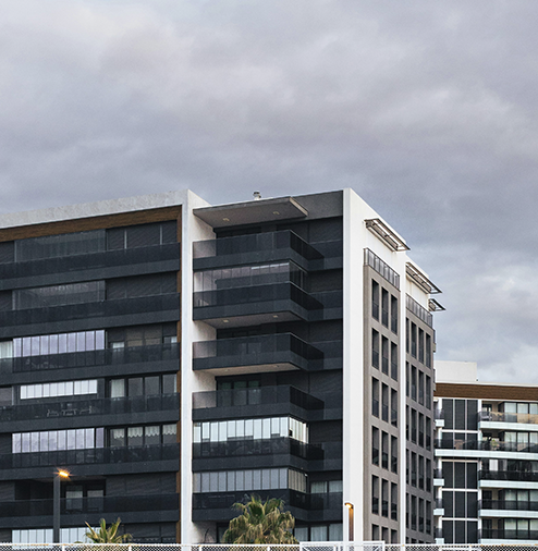 Modern multi-story residential or commercial building with glass windows and balconies, under a cloudy sky.