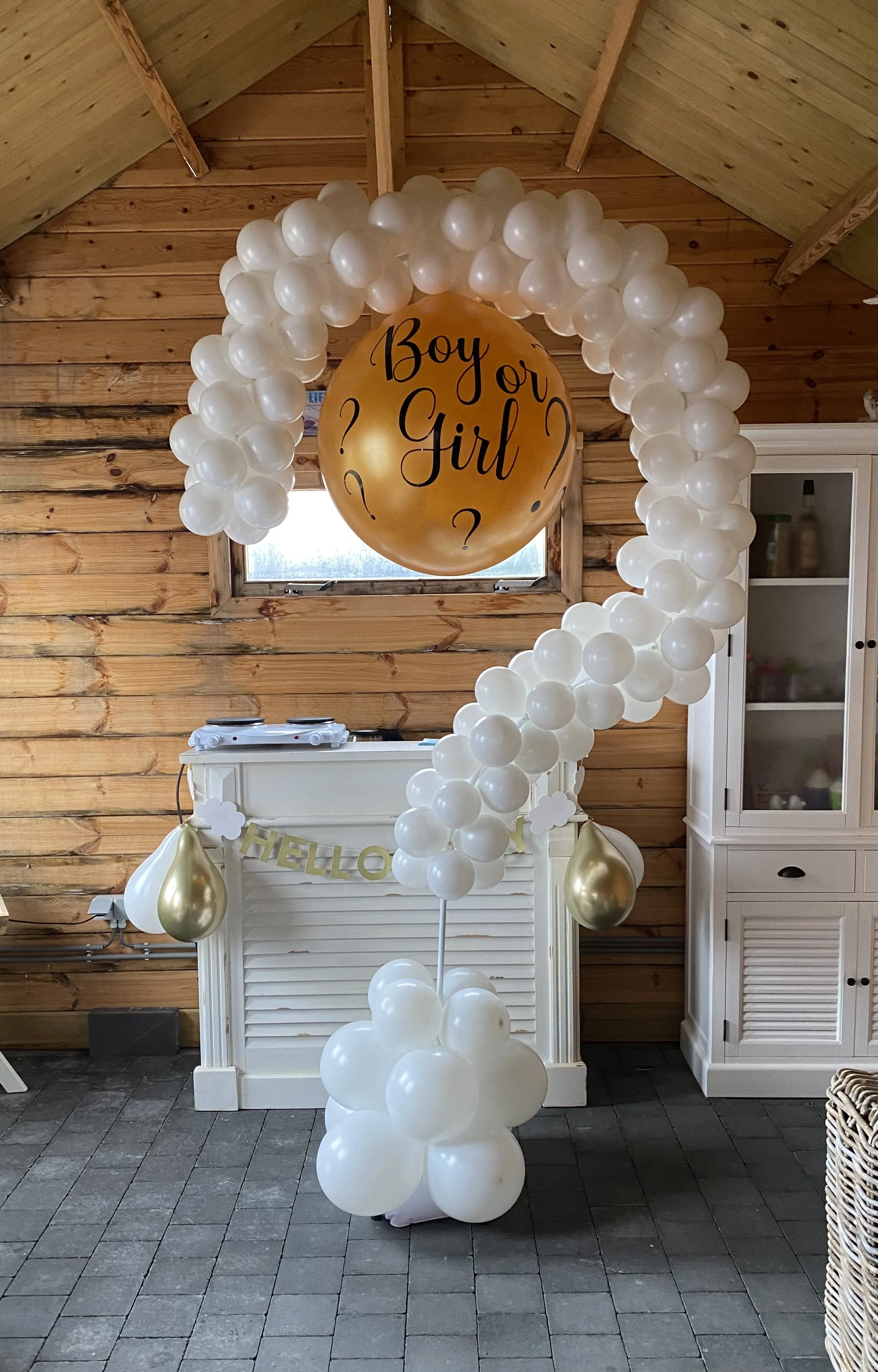 Decoraties met witte en gouden ballonnen, inclusief een grote gouden ballon met de tekst 'Boy or Girl?'.