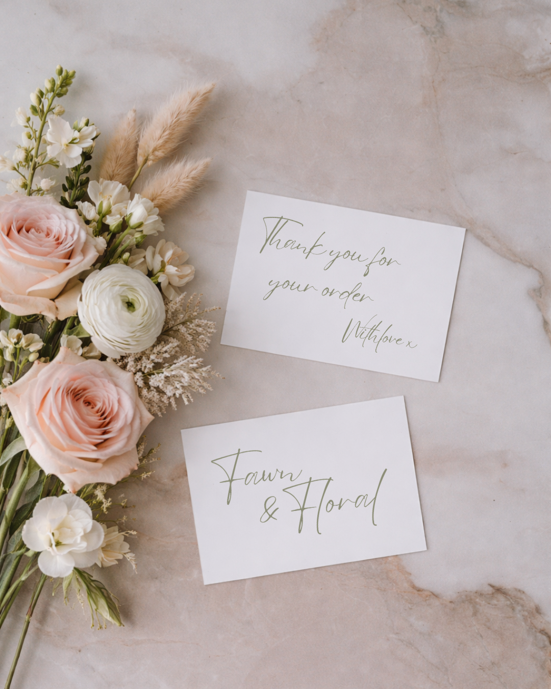 A bouquet of pink roses, white ranunculus, and various white and beige flowers with greenery, alongside two cards with handwritten-style text, one thanking for the order and the other indicating floral and herbal products, on a light marble surface.